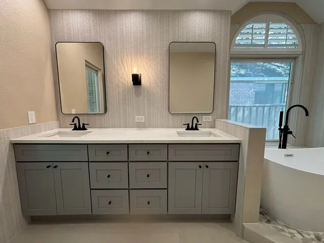Dual vanity with undermount sinks and matte black faucets, floating gray cabinetry, stone-finish countertop, and wall-mounted sconces