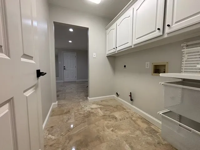 Laundry area featuring neutral-toned tile flooring, overhead white cabinetry, and a wall-mounted shelving system
