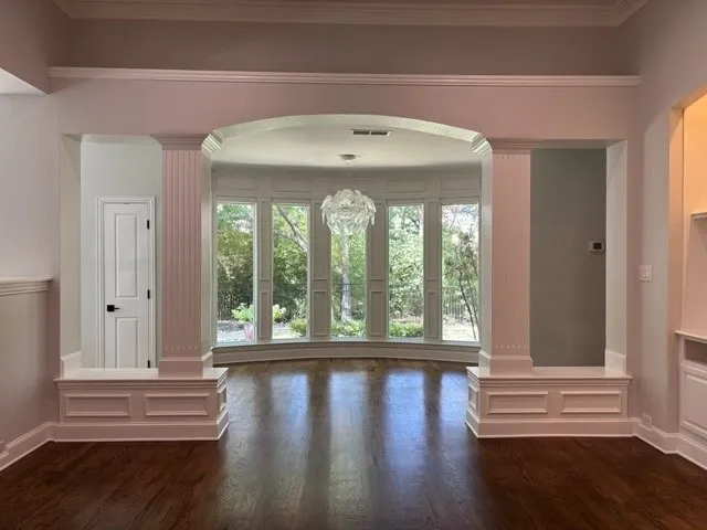 Wood-finish flooring, arched entryway, decorative columns, wainscoting, and large bay windows