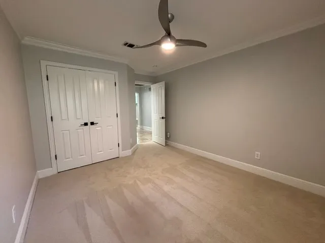Carpeted flooring, crown molding, double bi-fold doors, and a ceiling fan with integrated lighting