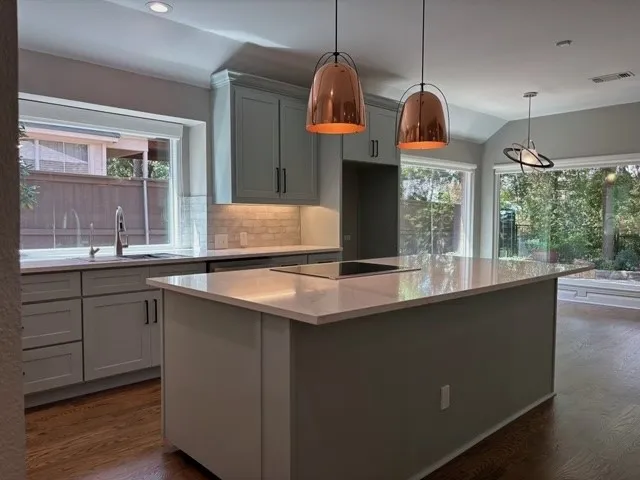 Kitchen featuring a large center island, light-toned countertops, integrated cooktop, pendant lighting, and hardwood flooring
