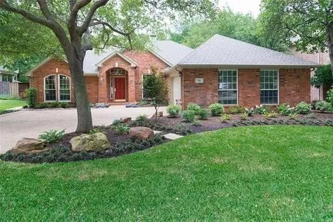 Brick exterior with a prominent arched entry, multiple windows, a paved driveway, and mature trees