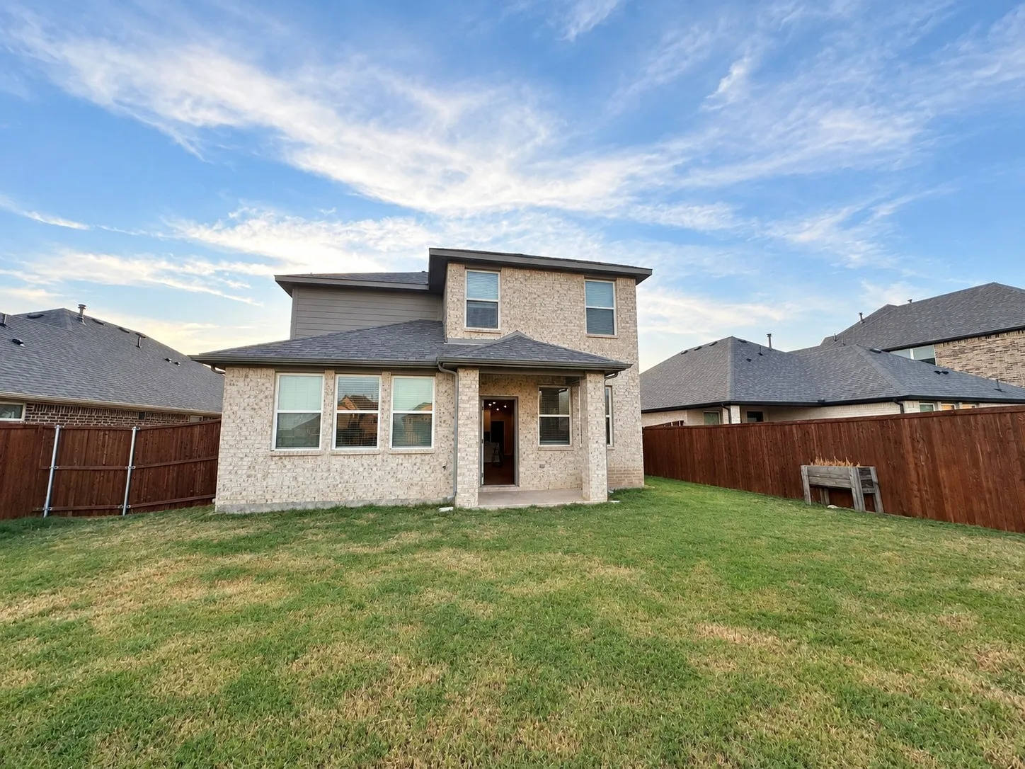 Expansive backyard with a manicured lawn, full privacy fencing, and a covered patio area
