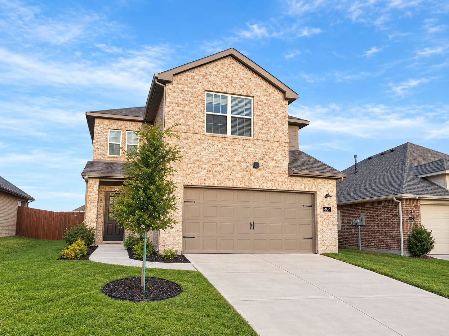 Brick exterior, attached two-car garage, concrete driveway, front walkway, and mature landscaping