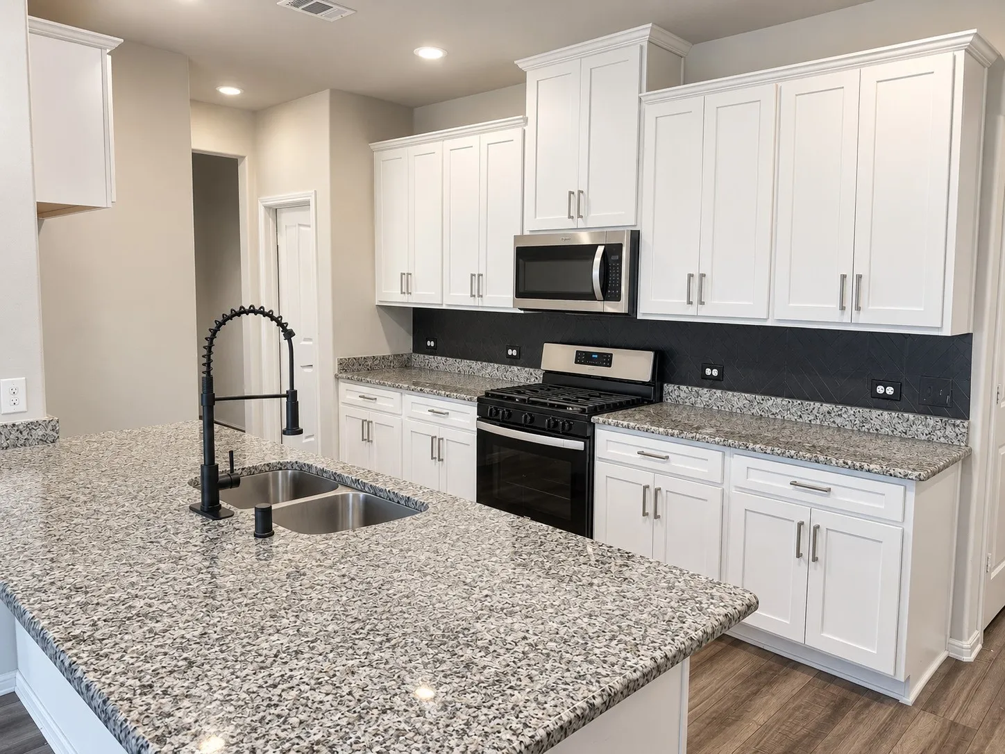 Kitchen featuring white shaker-style cabinetry, granite countertops, stainless steel appliances, a double basin sink, and a matte black pull-down faucet
