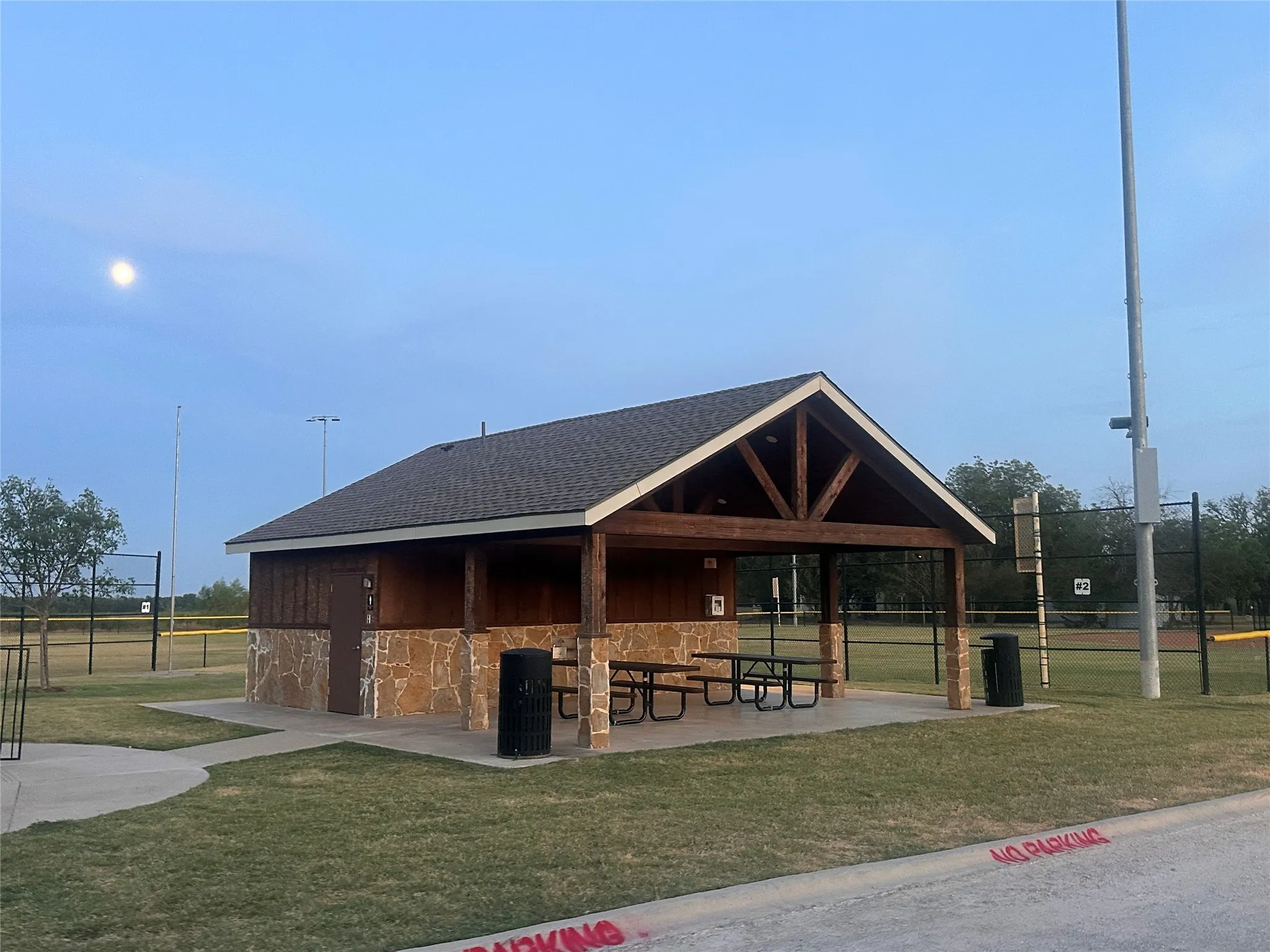 Gable roof structure with exposed wood beam detailing, stone veneer accents, wood-finish siding, and an integrated concrete patio