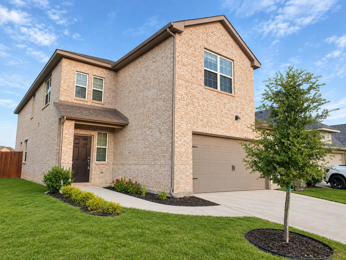 Two-story residence featuring a light-colored brick exterior, attached two-car garage, and a covered entry