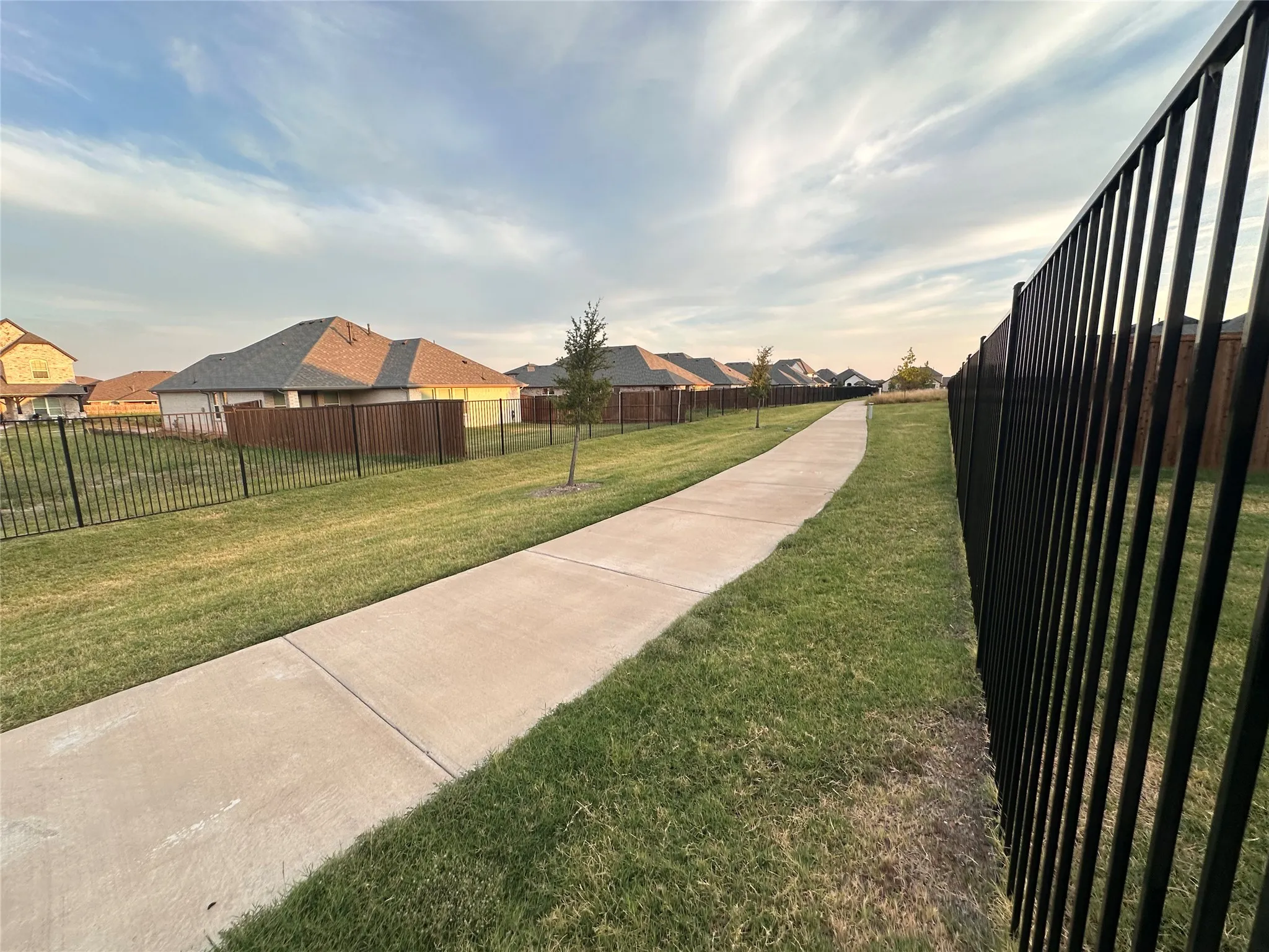 Concrete pathway with surrounding green space, bordered by a black metal fence