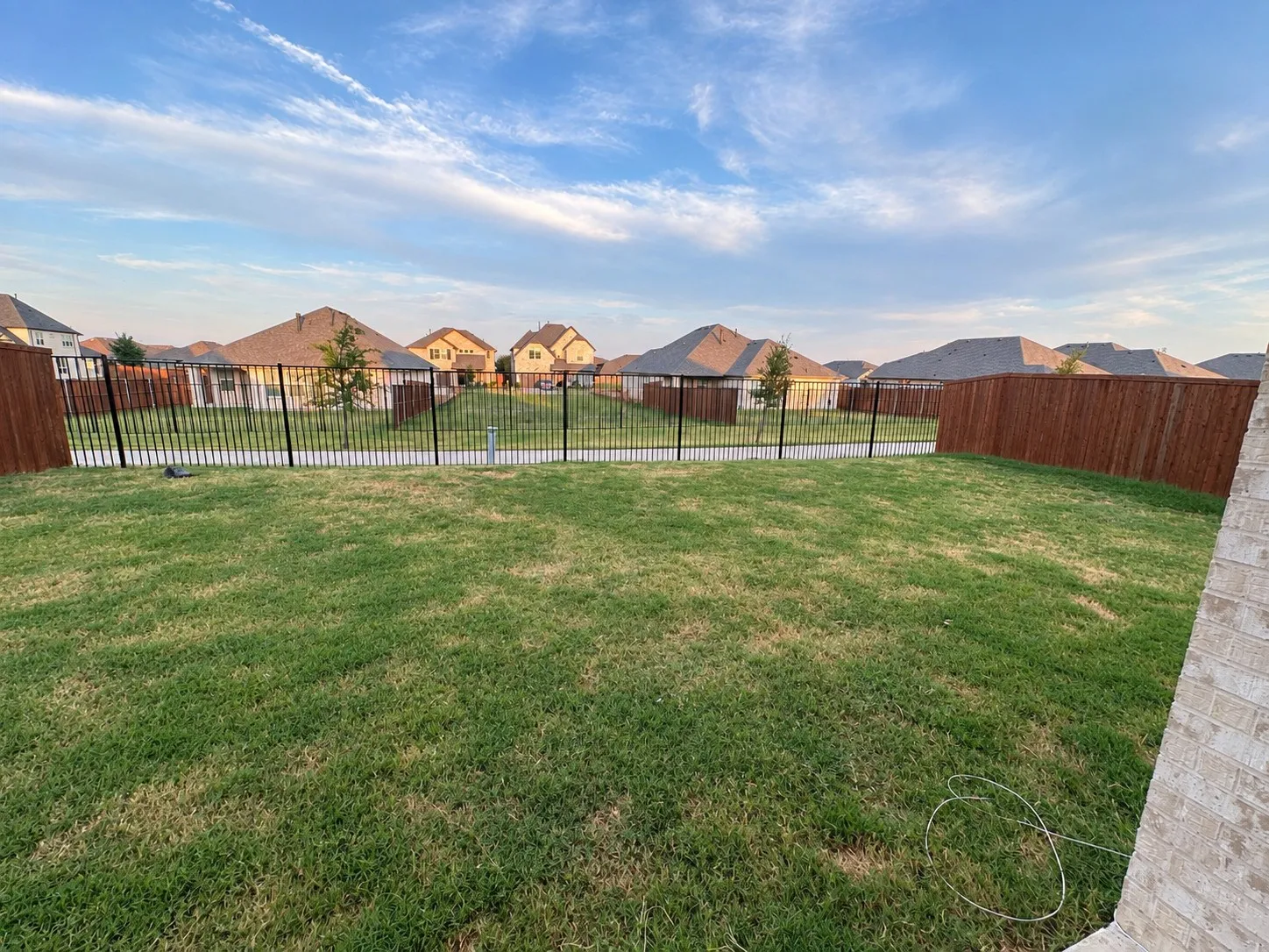 Expansive grassy yard with wood fencing and black metal fencing