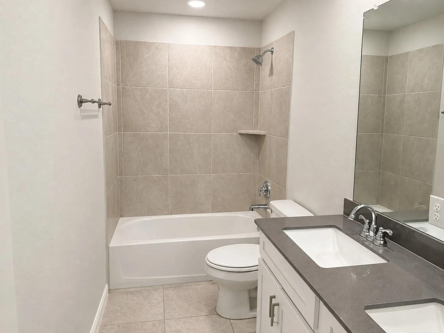 Bathroom featuring a white vanity with dual rectangular sinks, a dark countertop, chrome fixtures, and a tiled shower/tub combination with a built-in shelf