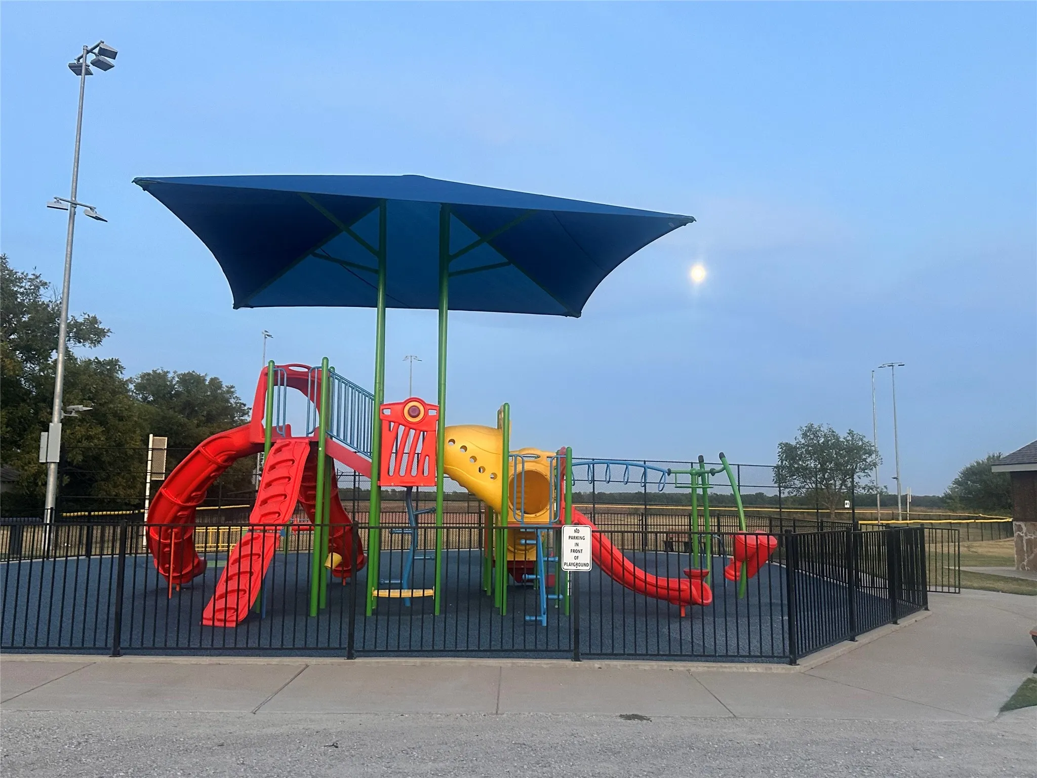Playground featuring a shade structure, protective fencing, rubberized ground surfacing, and a multi-component play​​‌​​​​‌​​‌‌​‌‌​​​‌‌​‌​‌​‌​​​‌​​ system