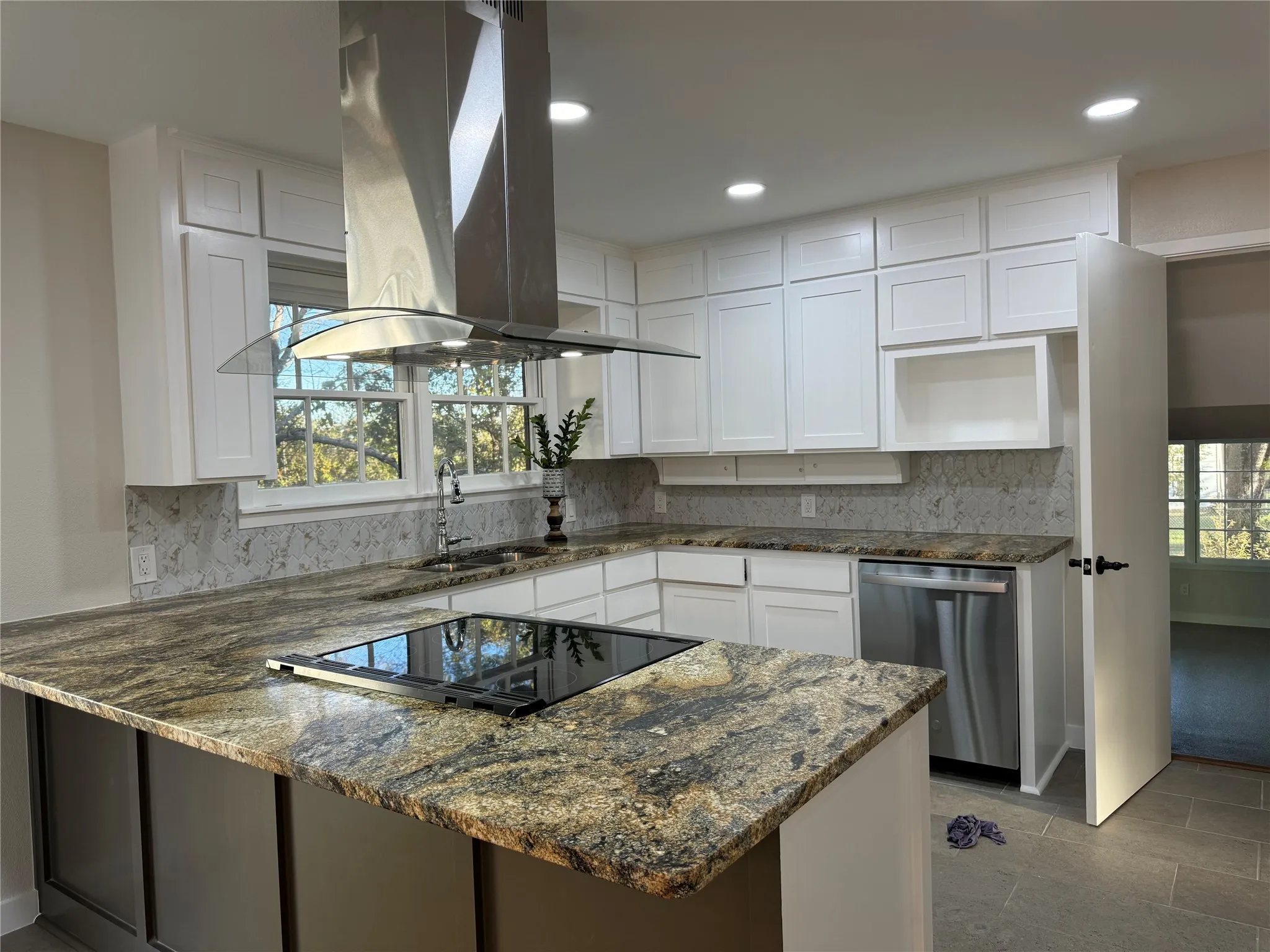 Kitchen with island range hood, kitchen peninsula, sink, stainless steel dishwasher, and white cabinetry