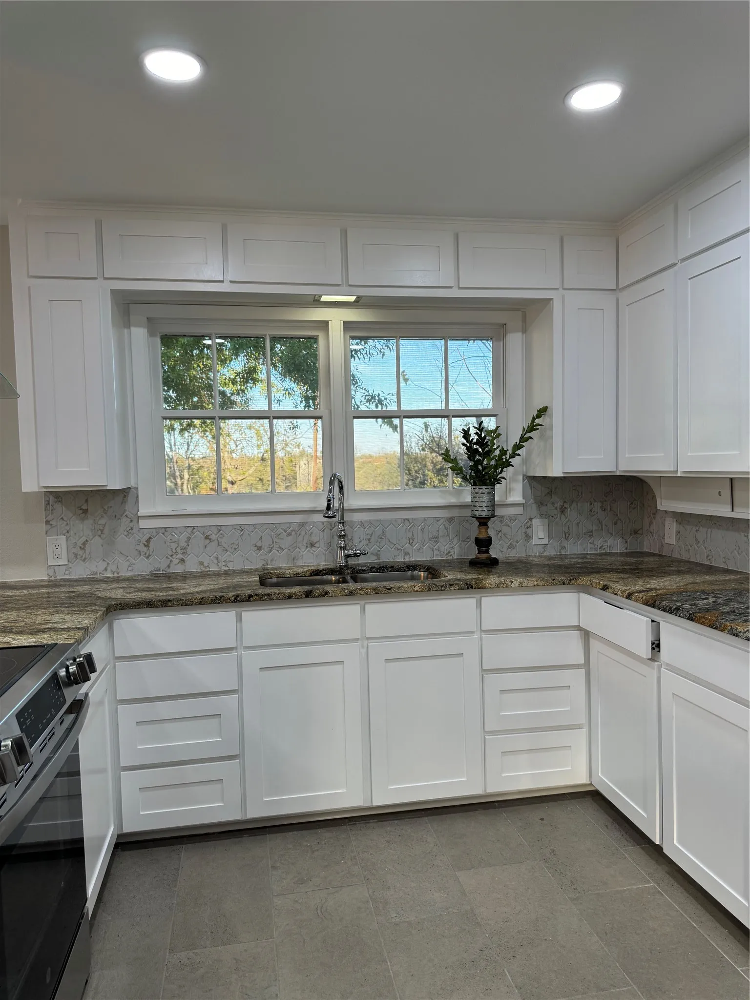 Kitchen with decorative backsplash, range, sink, white cabinetry, and dark stone countertops