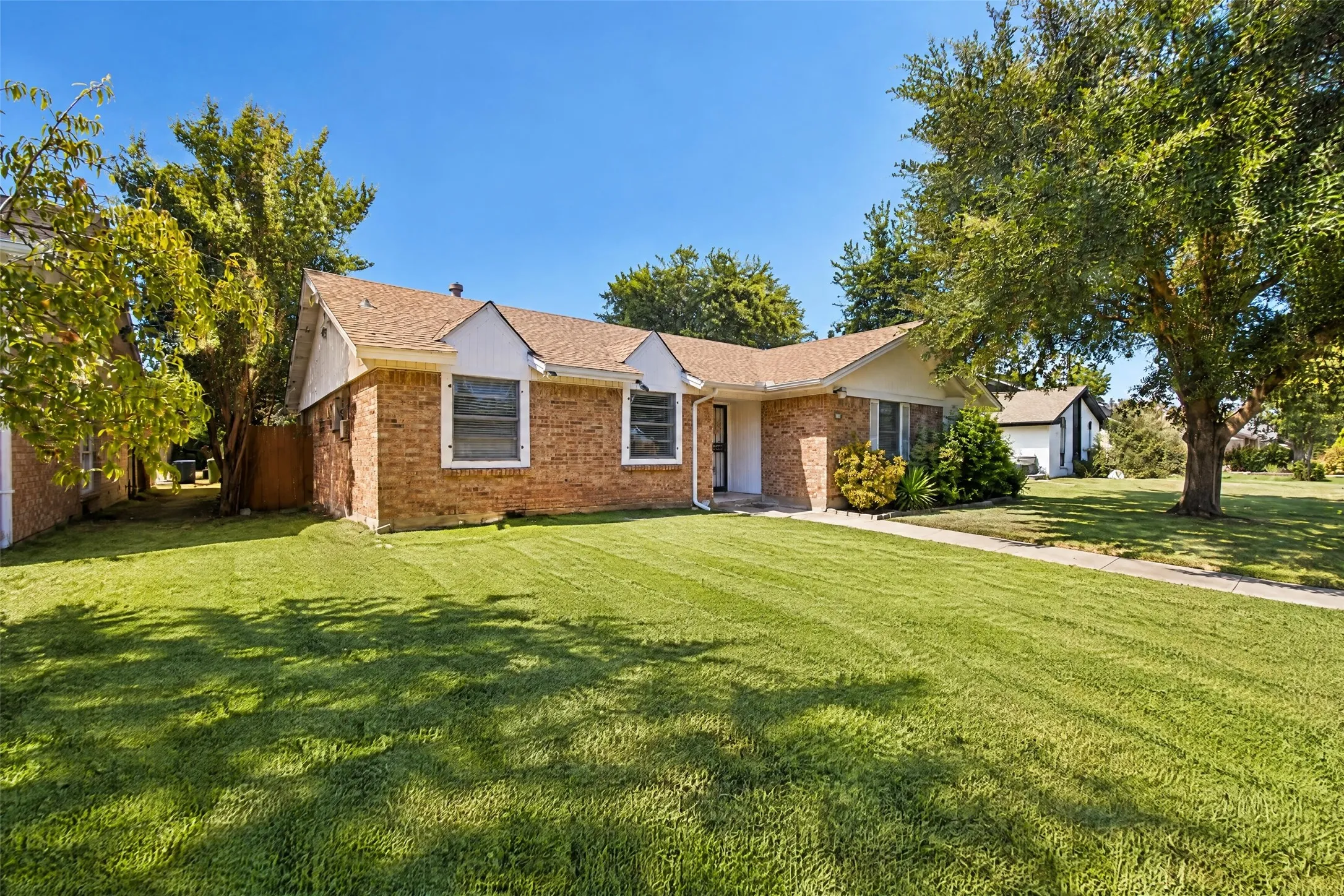 Brick exterior, gabled roofline, mature trees, and a concrete pathway