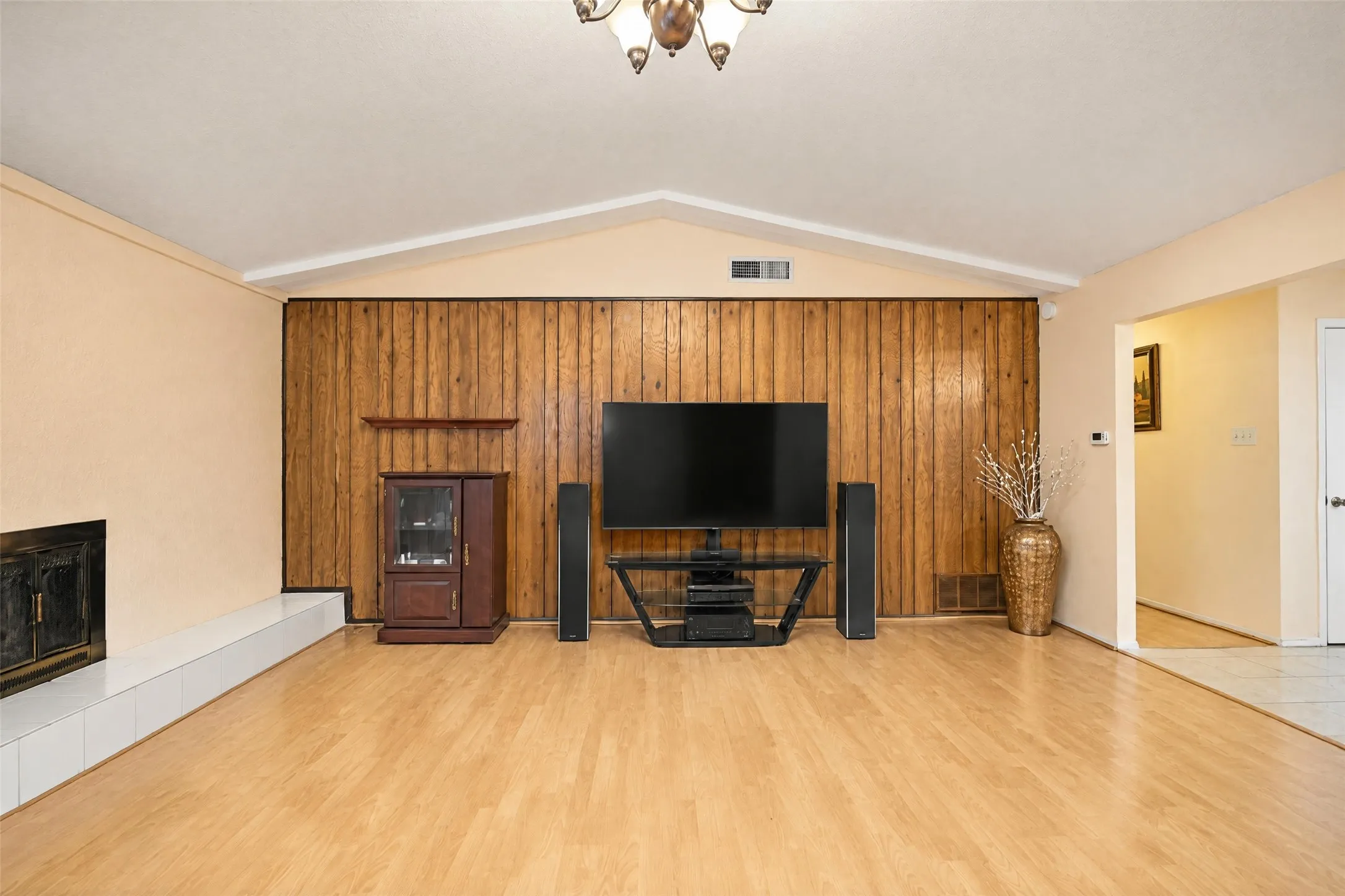 Vaulted ceiling, wood-finish flooring, fireplace with white tiled hearth, wood-paneled accent wall, and ceiling-mounted light fixture