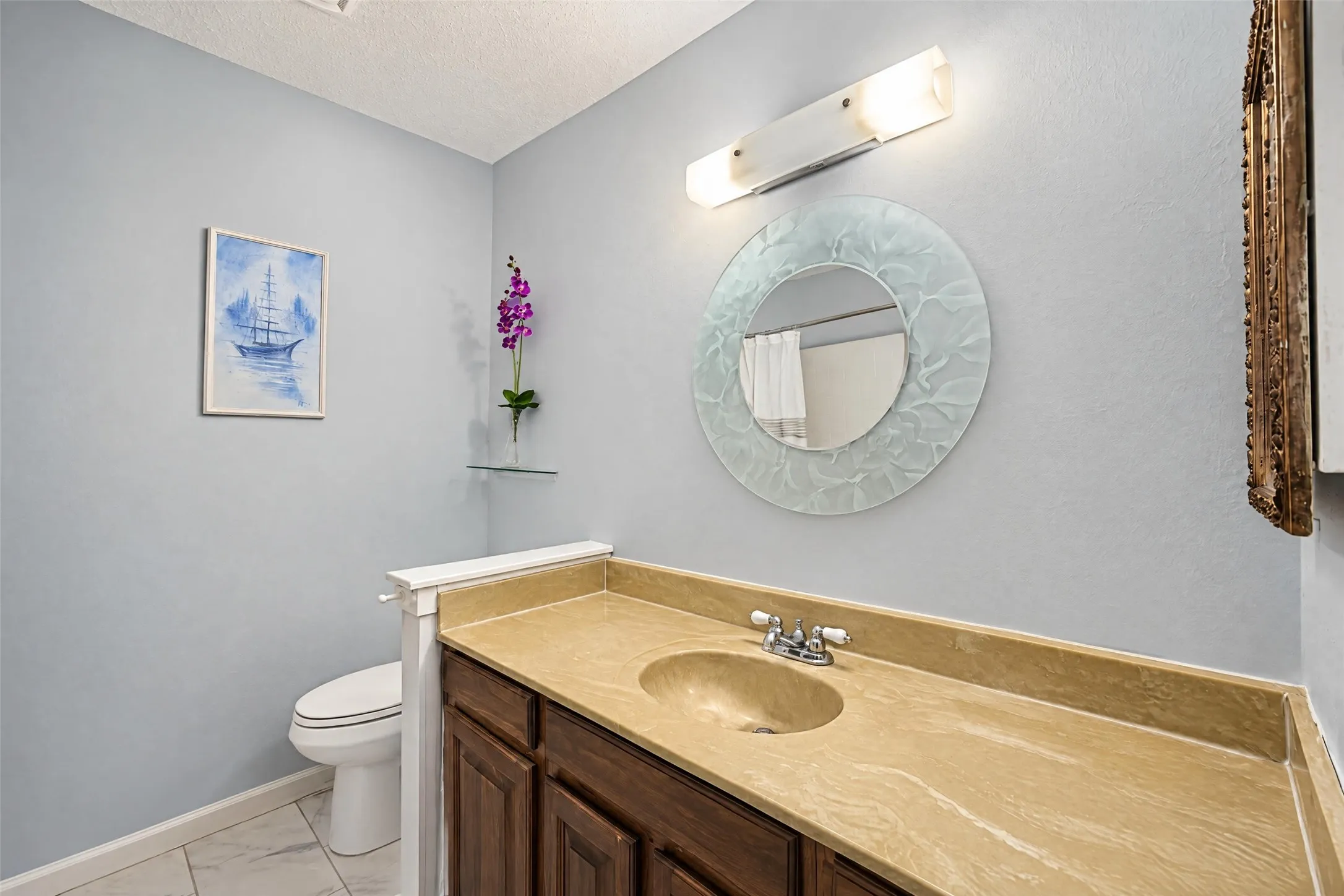 Vanity with an integrated sink and countertop, wood-finish cabinetry, and a circular wall mirror with a decorative frame