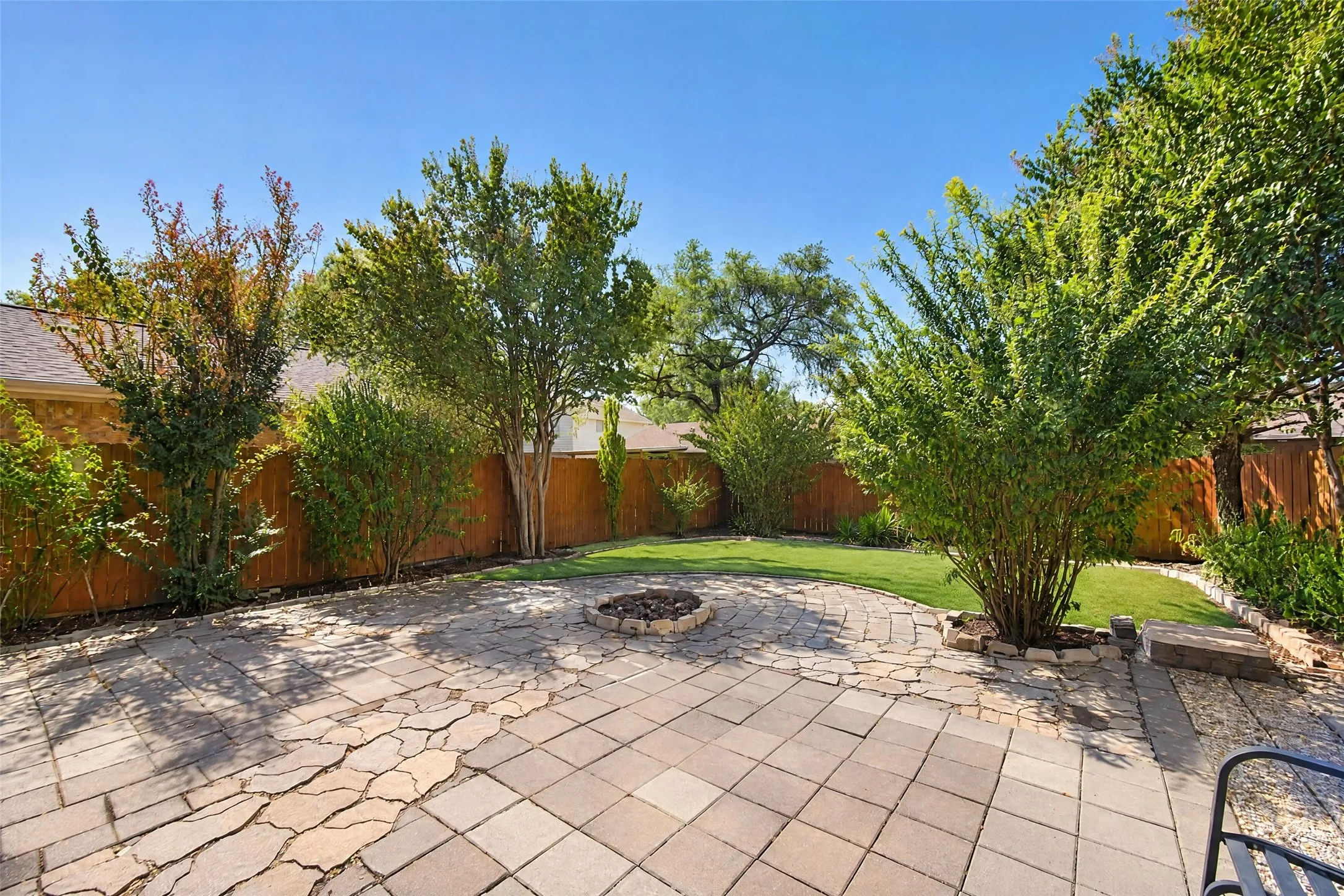 Expansive backyard featuring a paver patio, flagstone pathway, a built-in fire pit, manicured lawn, and mature trees