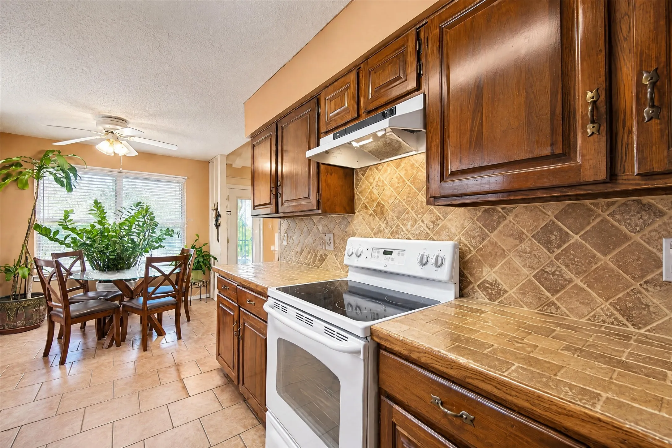 Kitchen with wood cabinetry, tile countertops, and a tile backsplash