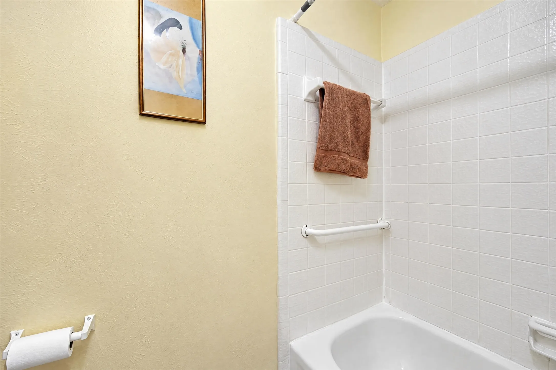 Bathtub with white subway tile surround, integrated grab bar, and wall-mounted towel rack