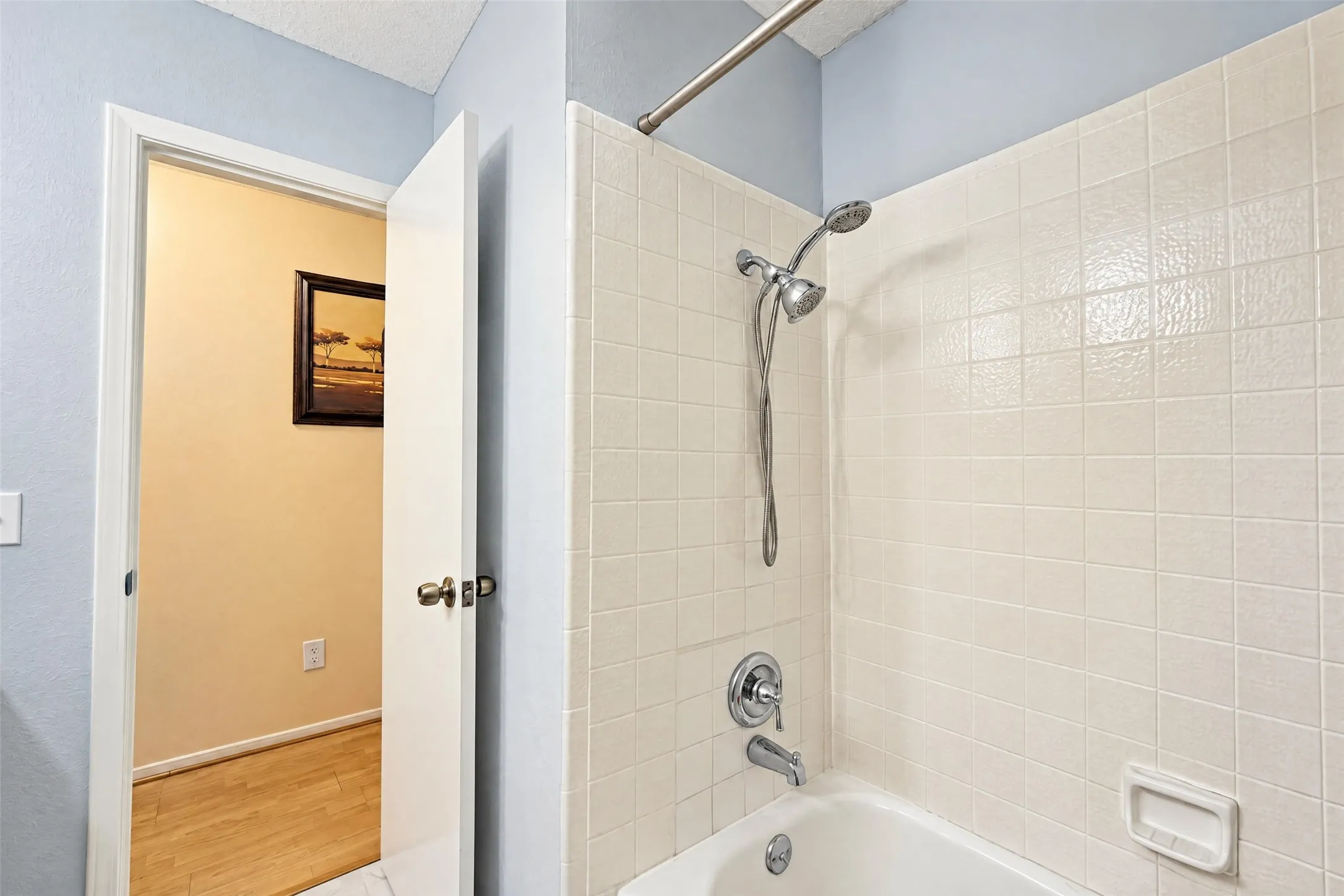 White tiled shower surround with a fixed showerhead and handheld sprayer, and a white bathtub