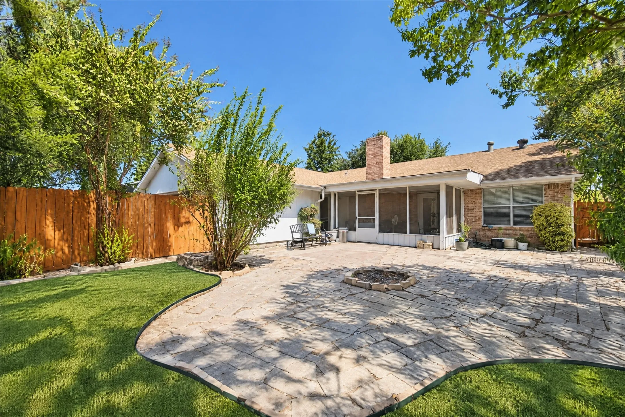 Expansive backyard featuring a stone paver patio with a built-in fire pit, manicured lawn, screened-in porch, and a brick exterior