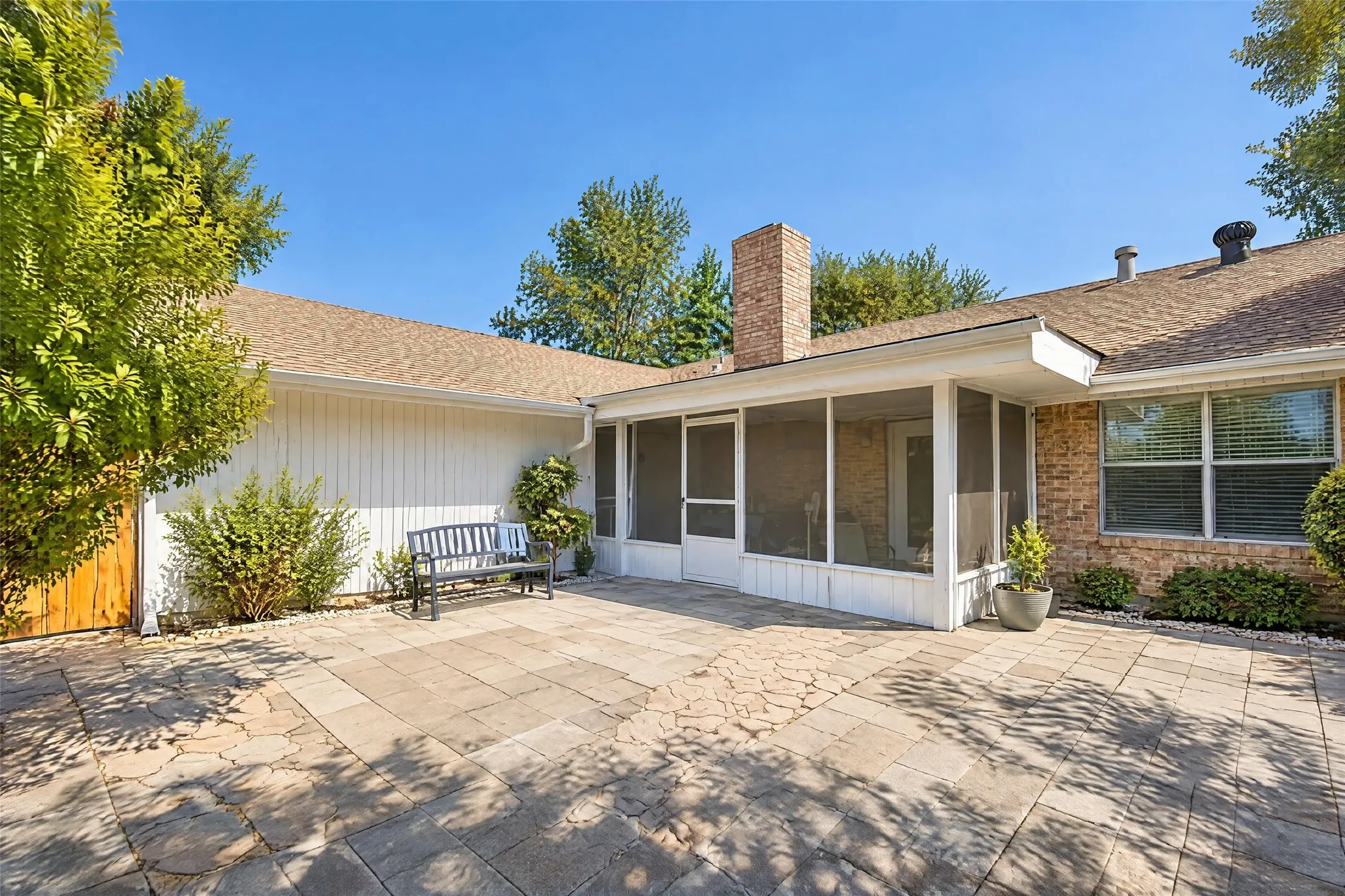 Expansive paver patio with a screened-in porch, brick exterior, and a prominent brick chimney