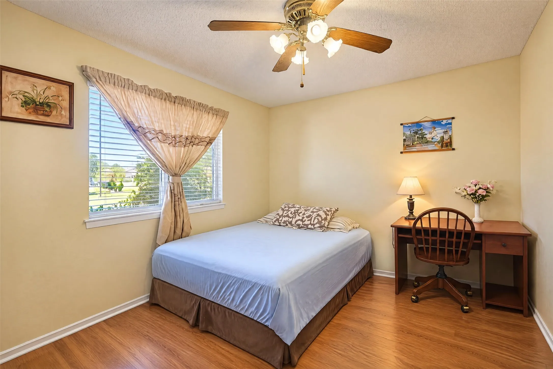 Wood-finish flooring, neutral wall tones, window with horizontal blinds, and a ceiling fan with integrated lighting