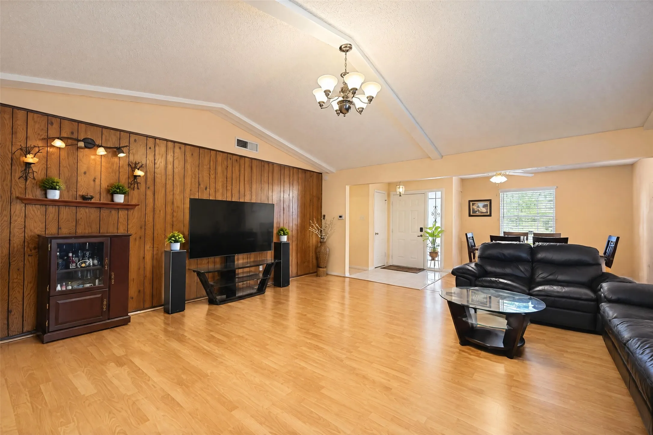 Vaulted ceiling with exposed beams, wood-finish flooring, wood panel accent wall, recessed entry, and a ceiling fan