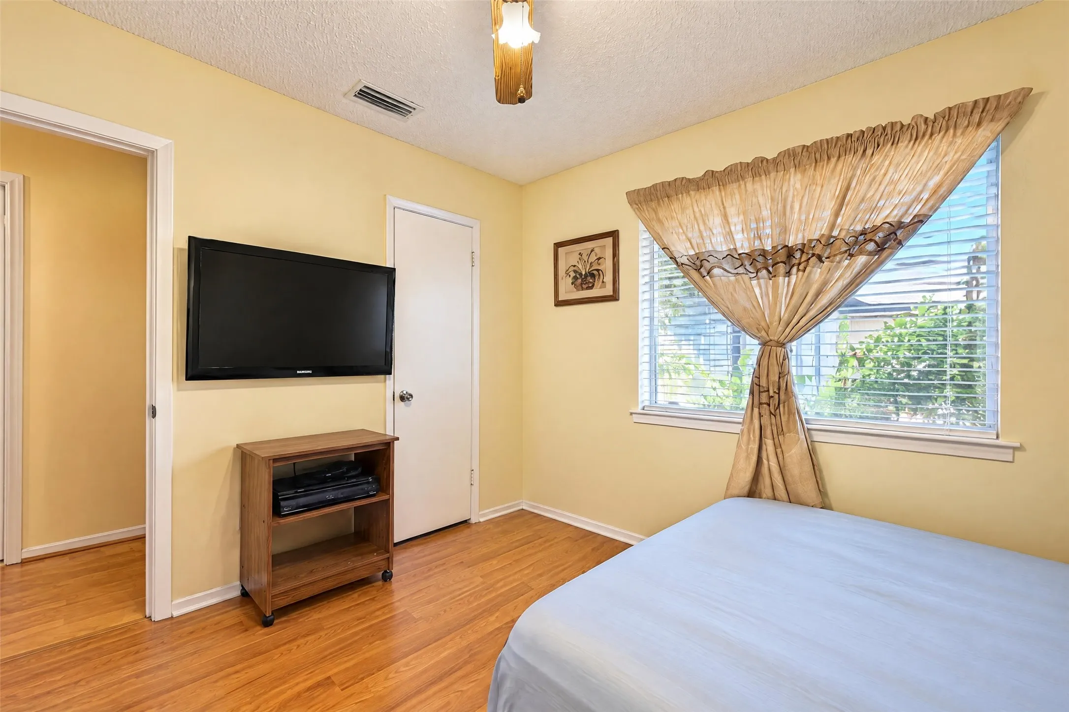 Wood-finish flooring with light-toned walls, featuring a window with blinds