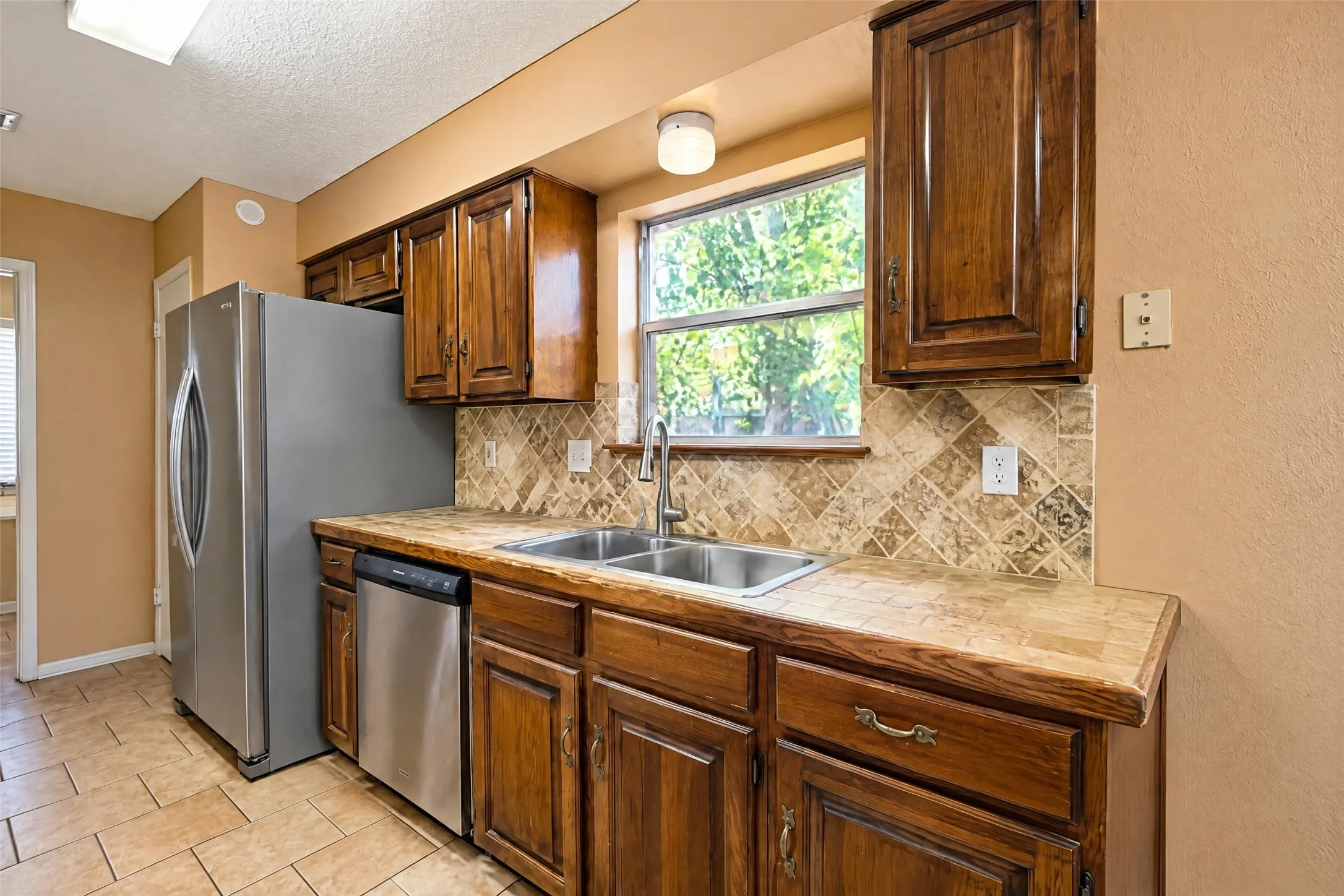 Wood cabinetry with tile countertops, stainless steel appliances, and a tiled backsplash