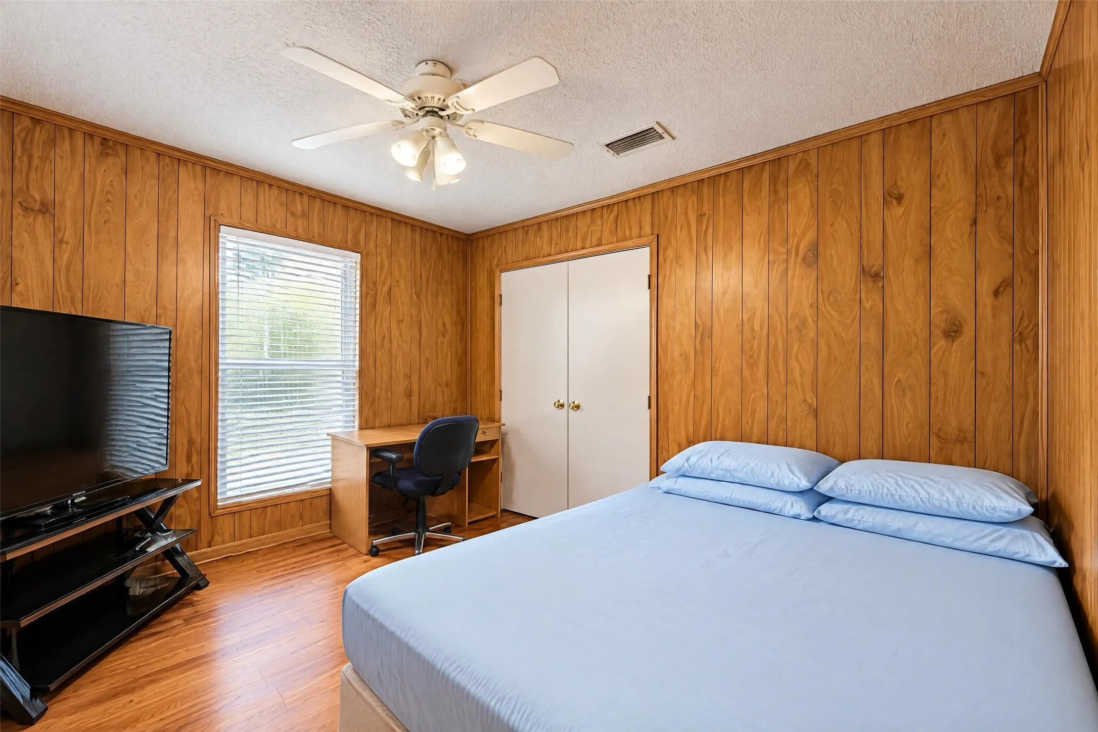 Wood-paneled wall finishes, wood-finish flooring, white ceiling fan with integrated lighting, white window blinds, and white bi-fold closet doors