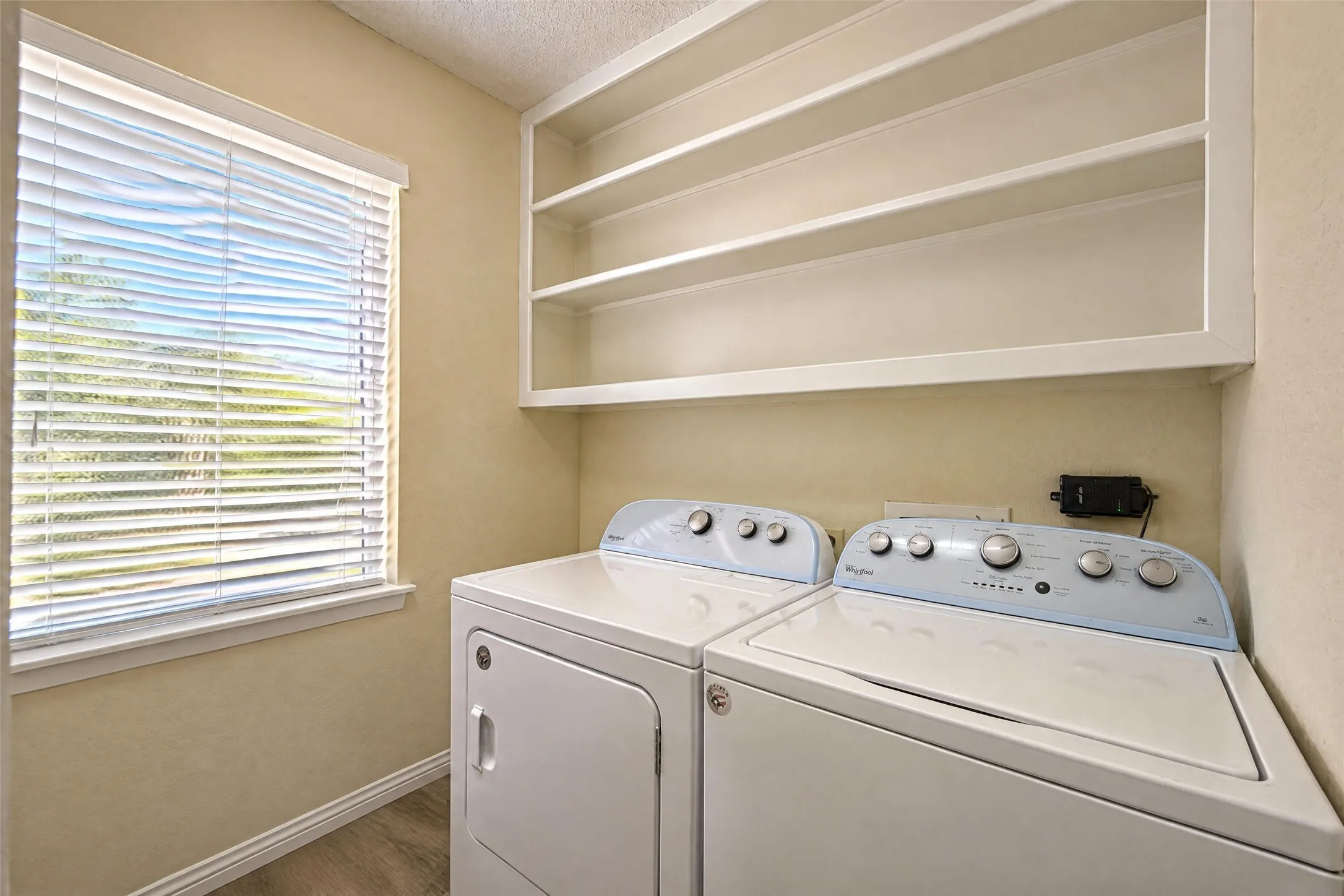 Laundry area featuring a window with blinds, open shelving, and wood-finish flooring