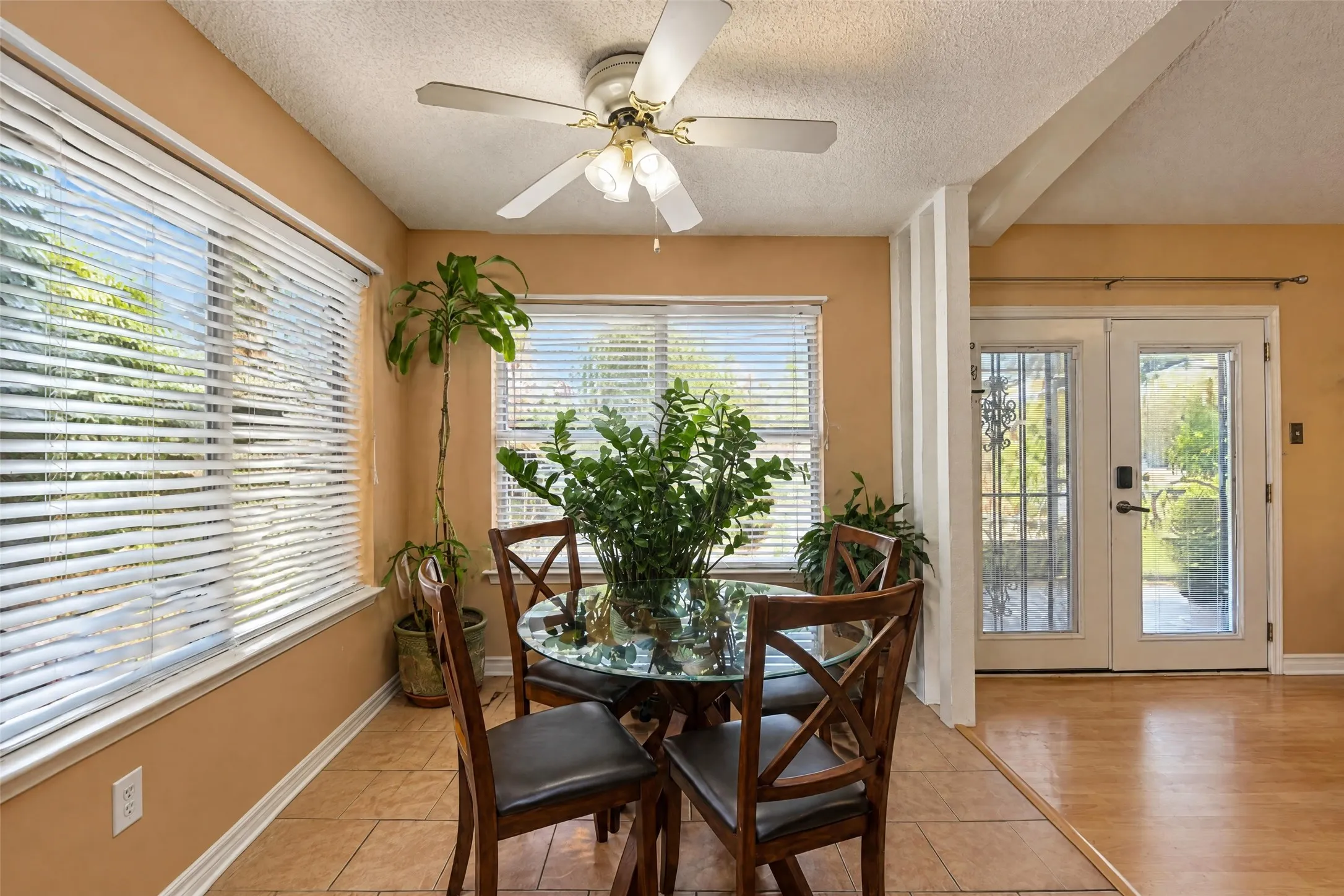 Ceiling fan with light kit, multiple windows with blinds, tiled flooring, wood-finish flooring, and double glass-paneled doors with security bars