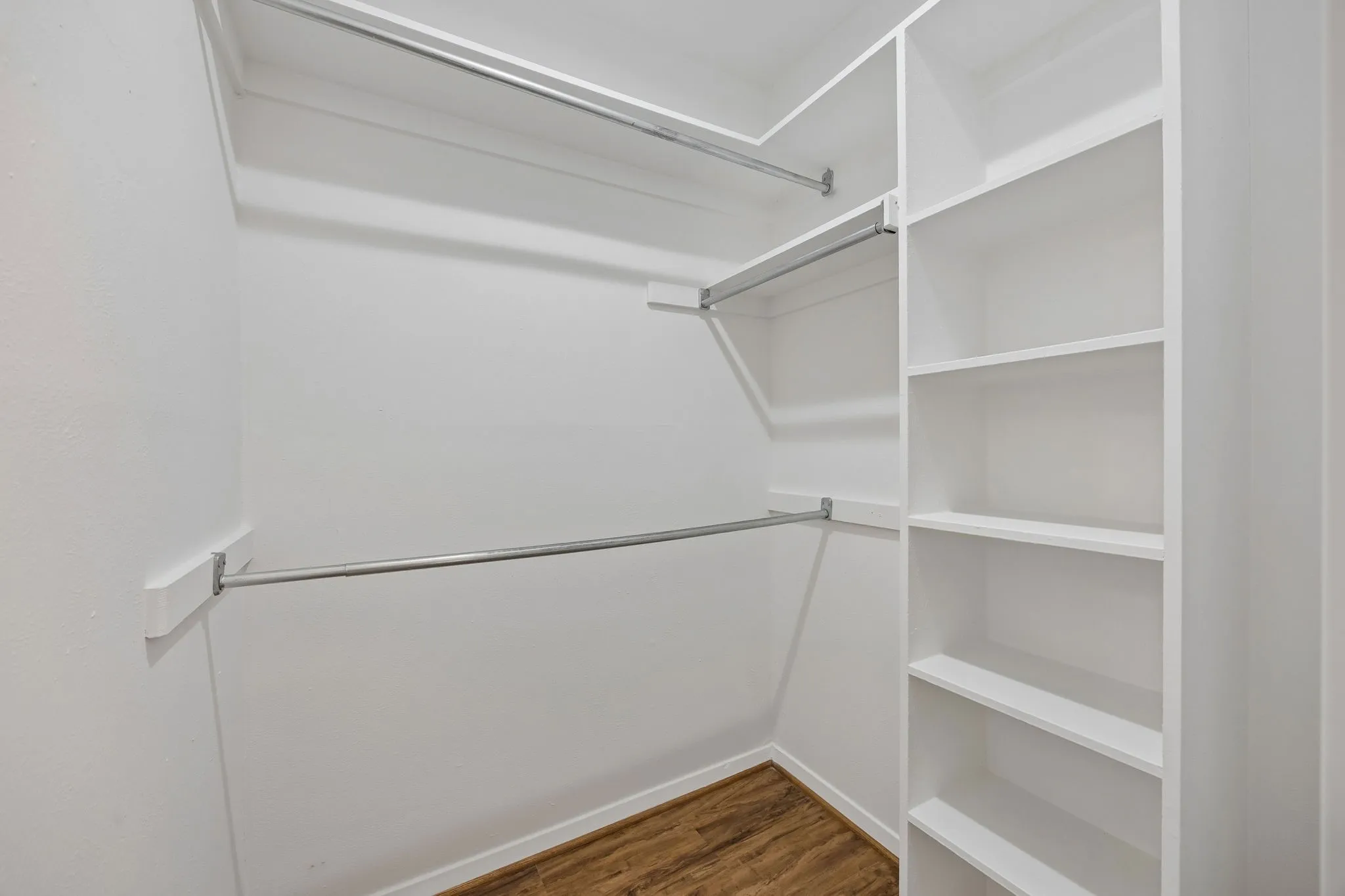 Built-in shelving, multiple hanging rods, and wood-finish flooring