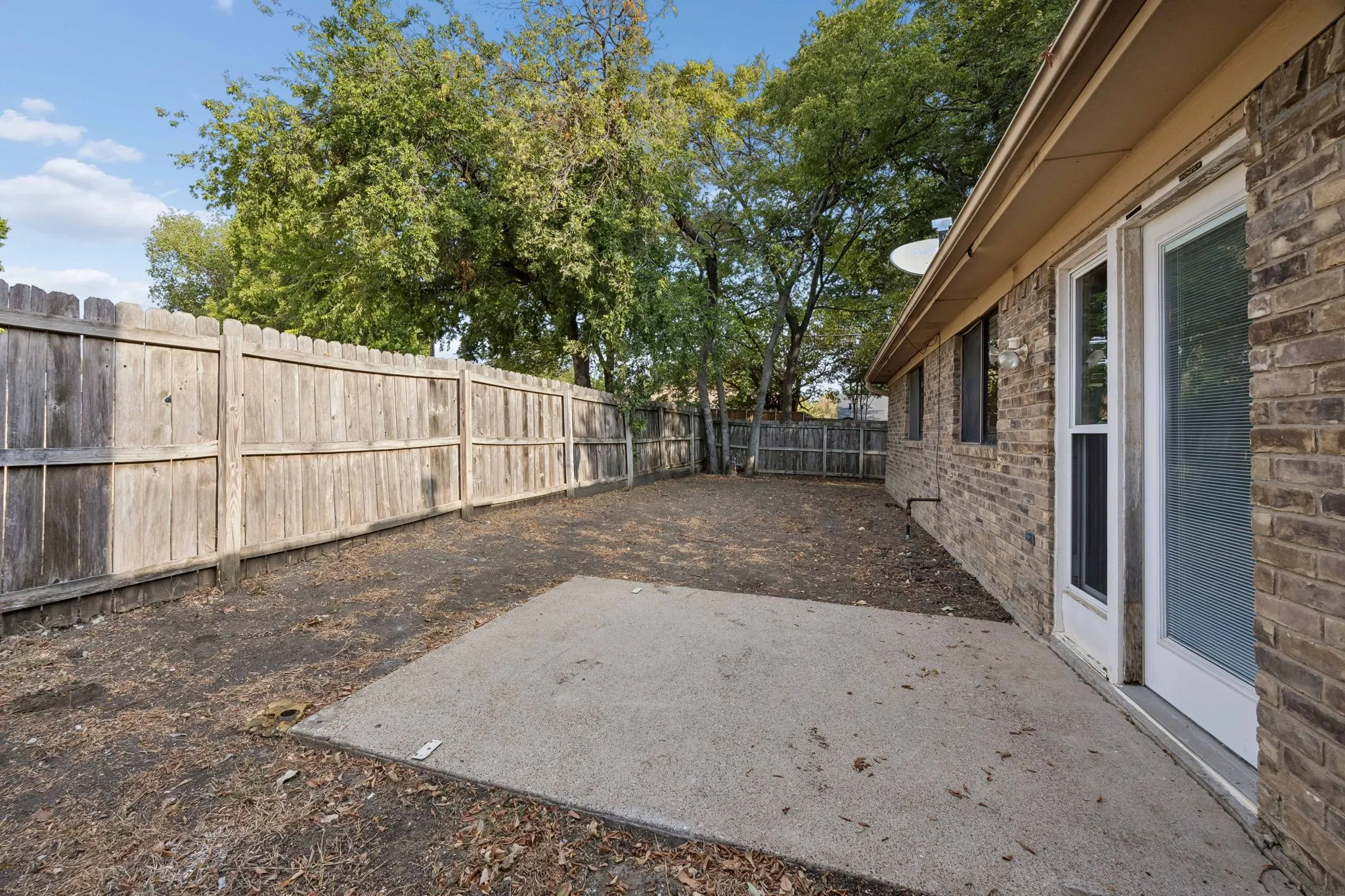 Brick exterior with a concrete patio pad, privacy fencing, and mature trees