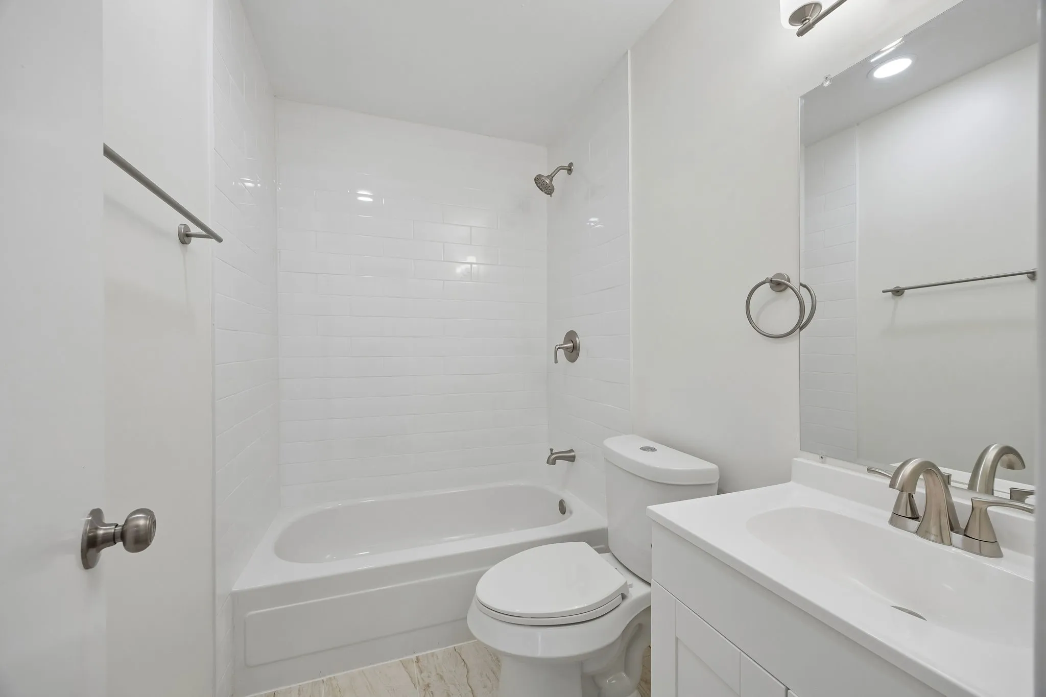 White subway tile surround, white vanity with integrated sink, brushed nickel fixtures, and light-toned flooring