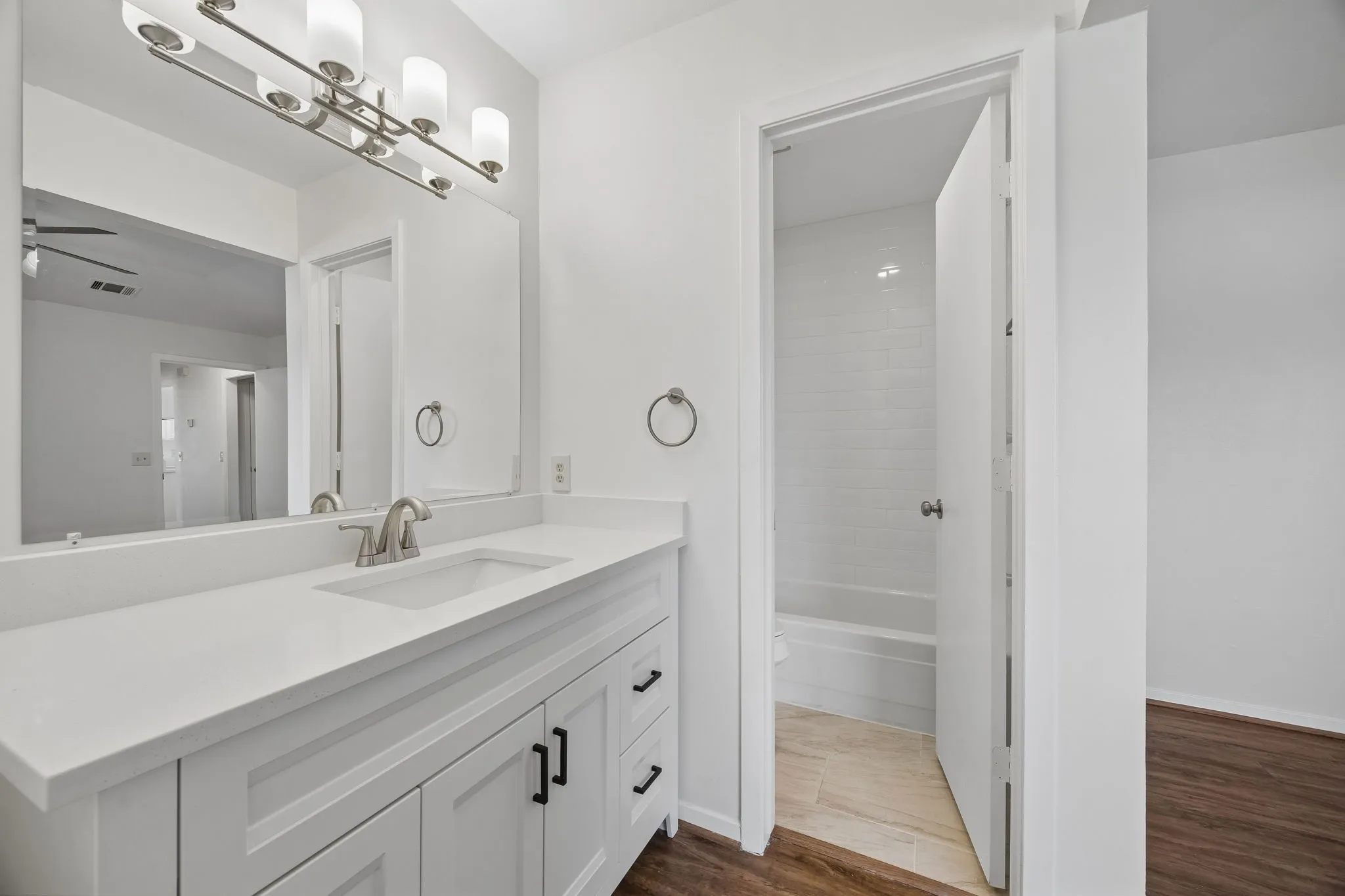 White shaker-style vanity with dark hardware, a rectangular undermount sink, and a spacious white countertop