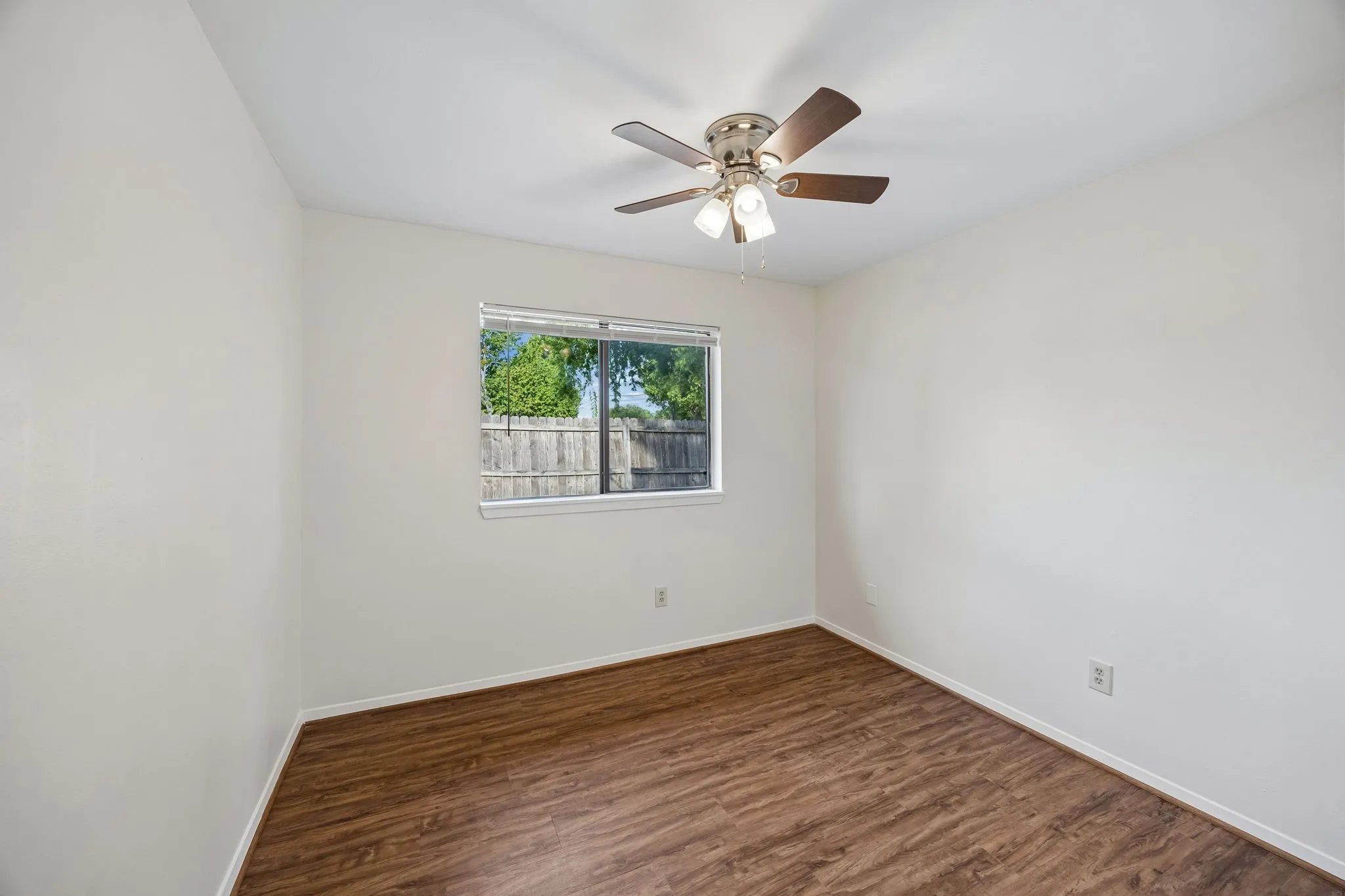 Neutral wall paint, wood-finish flooring, ceiling fan with integrated lighting, and a single pane window