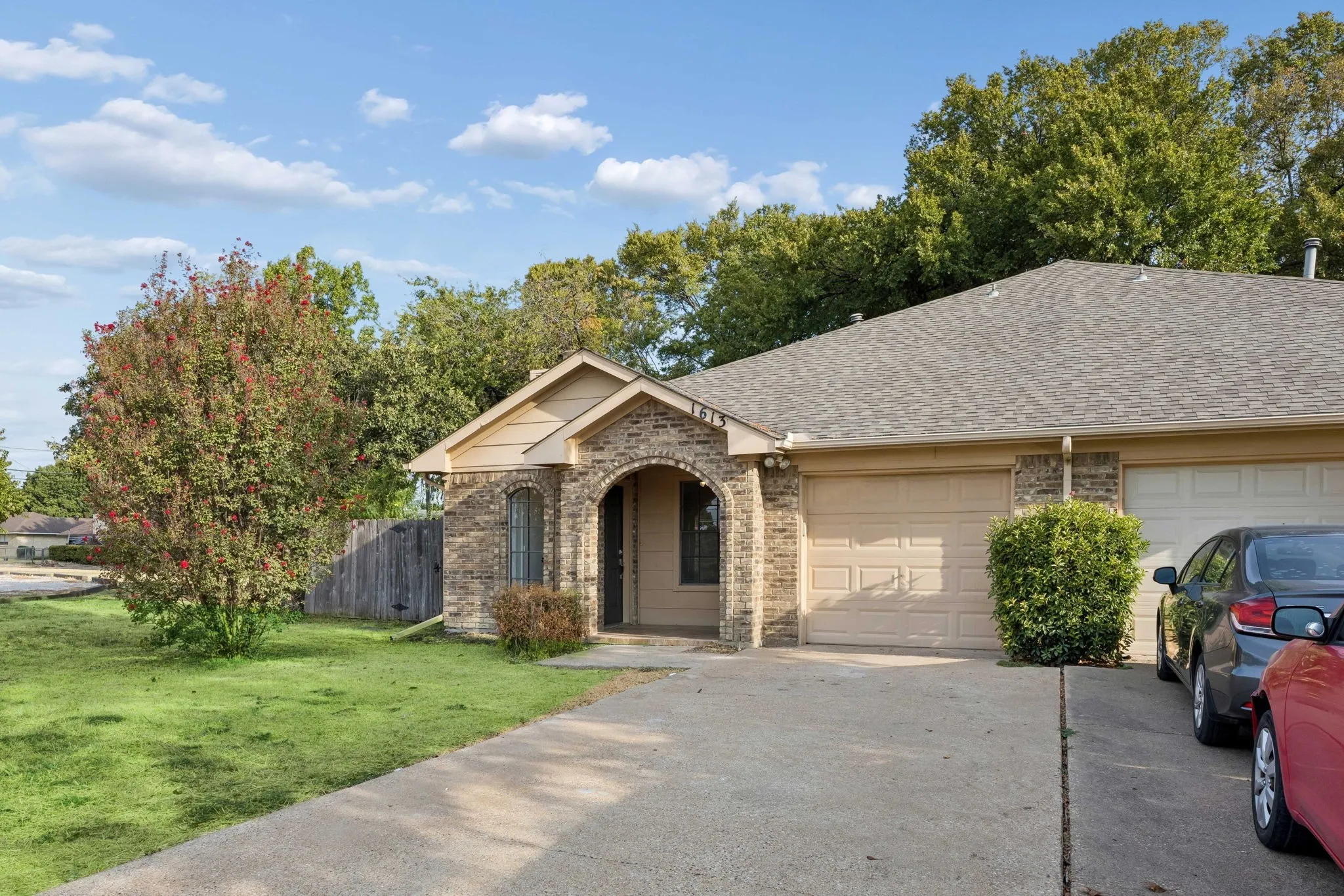 Stone facade with an arched entry, a concrete driveway, a shingle roof, and a mature tree