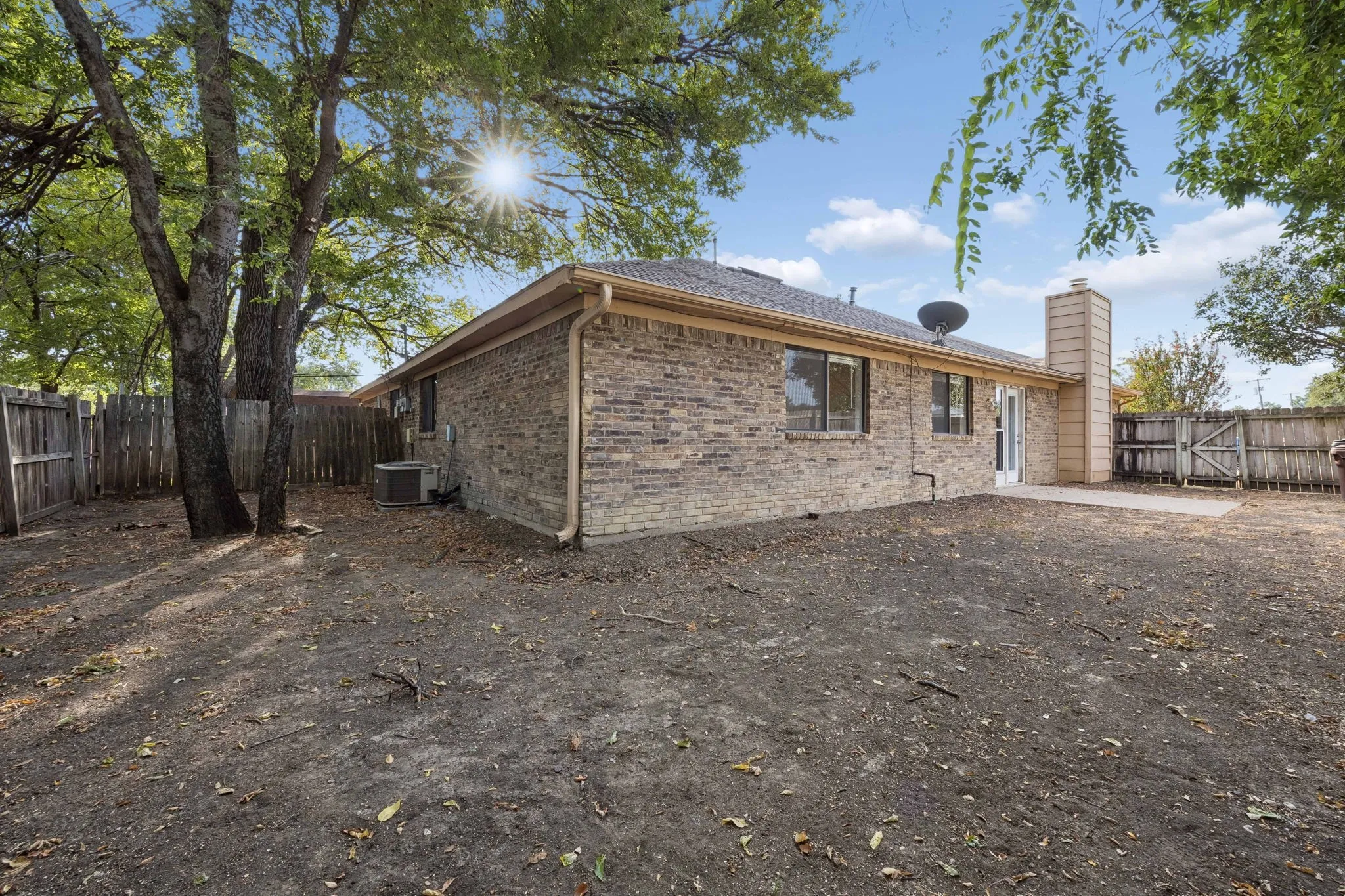 Brick exterior, multiple windows, a concrete patio, a wood fence, and mature trees