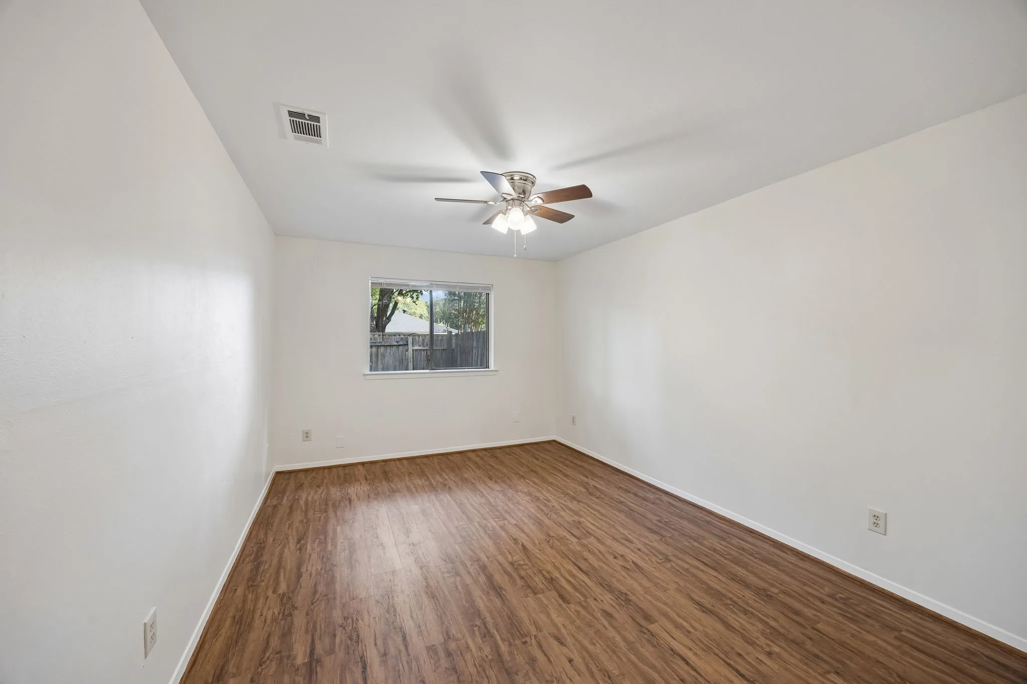 Wood-finish flooring, ceiling fan with integrated lighting, and a window with exterior views