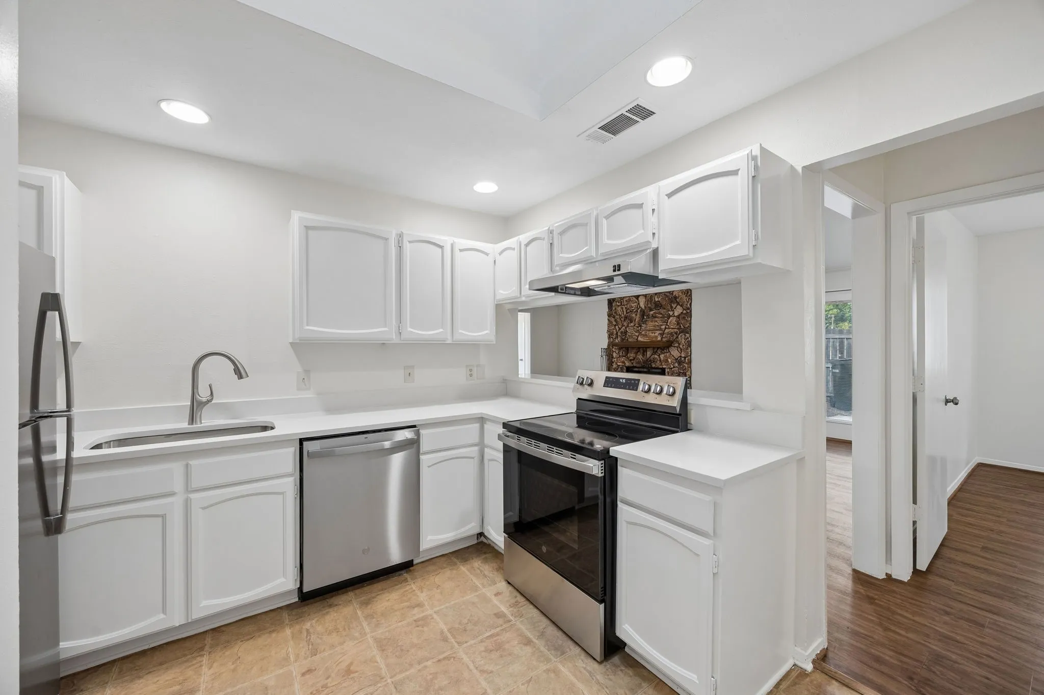 Stainless steel appliances, white cabinetry, recessed lighting, and a skylight illuminate this kitchen space