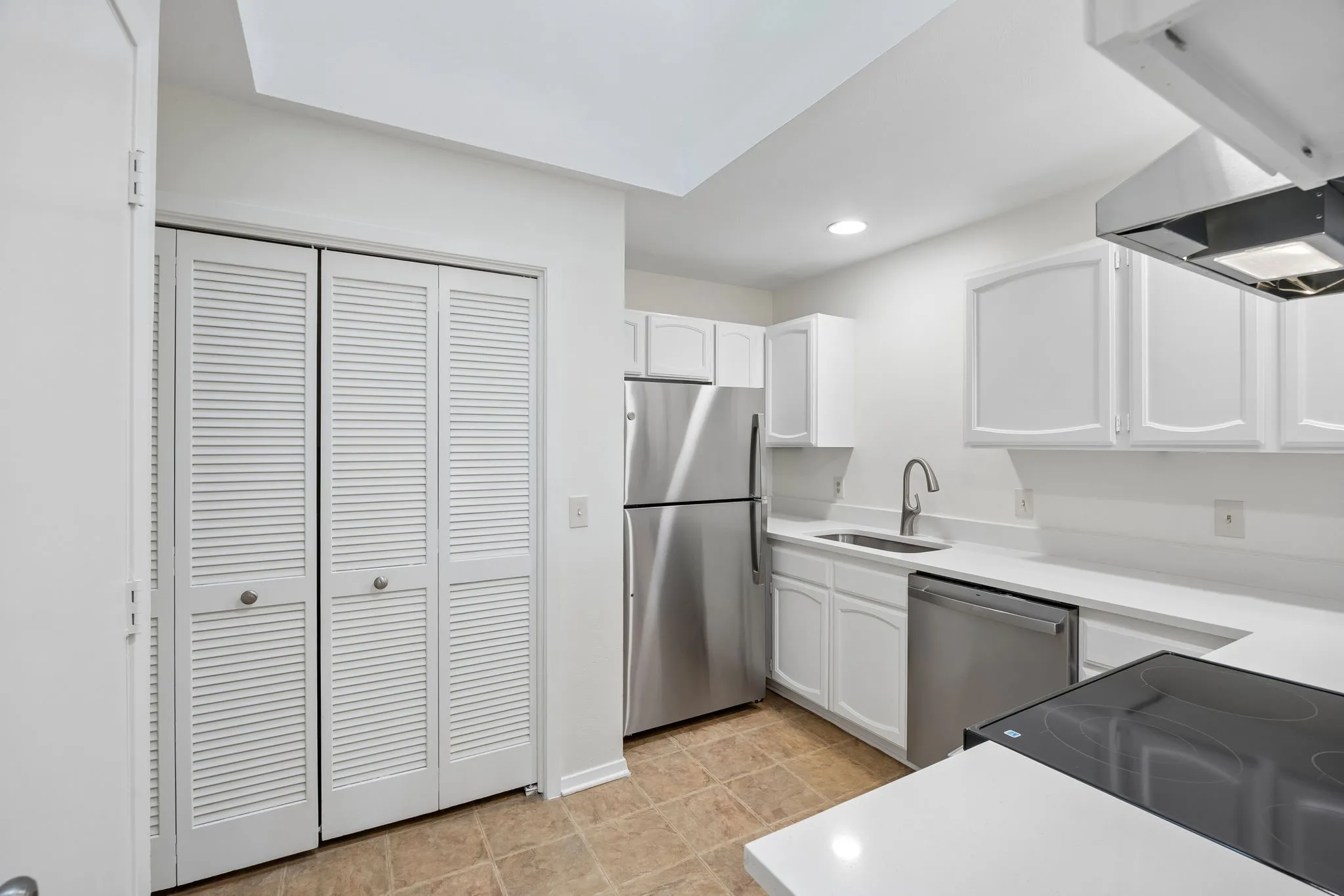 White cabinetry with brushed nickel hardware, stainless steel appliances, solid surface countertops, a stainless steel sink with a gooseneck faucet, and tile flooring
