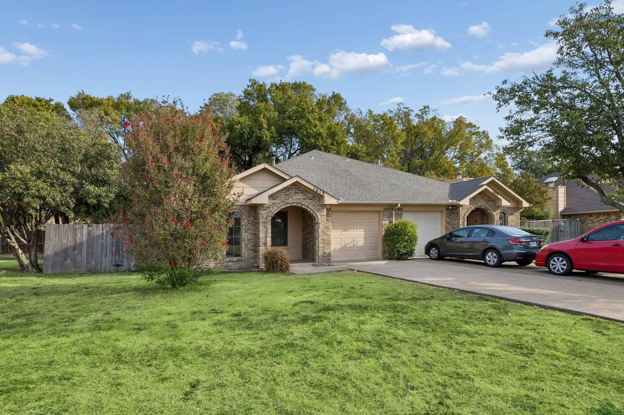 Exterior featuring a brick and siding facade, arched entryways, a shingle roof, and an attached one-car garage