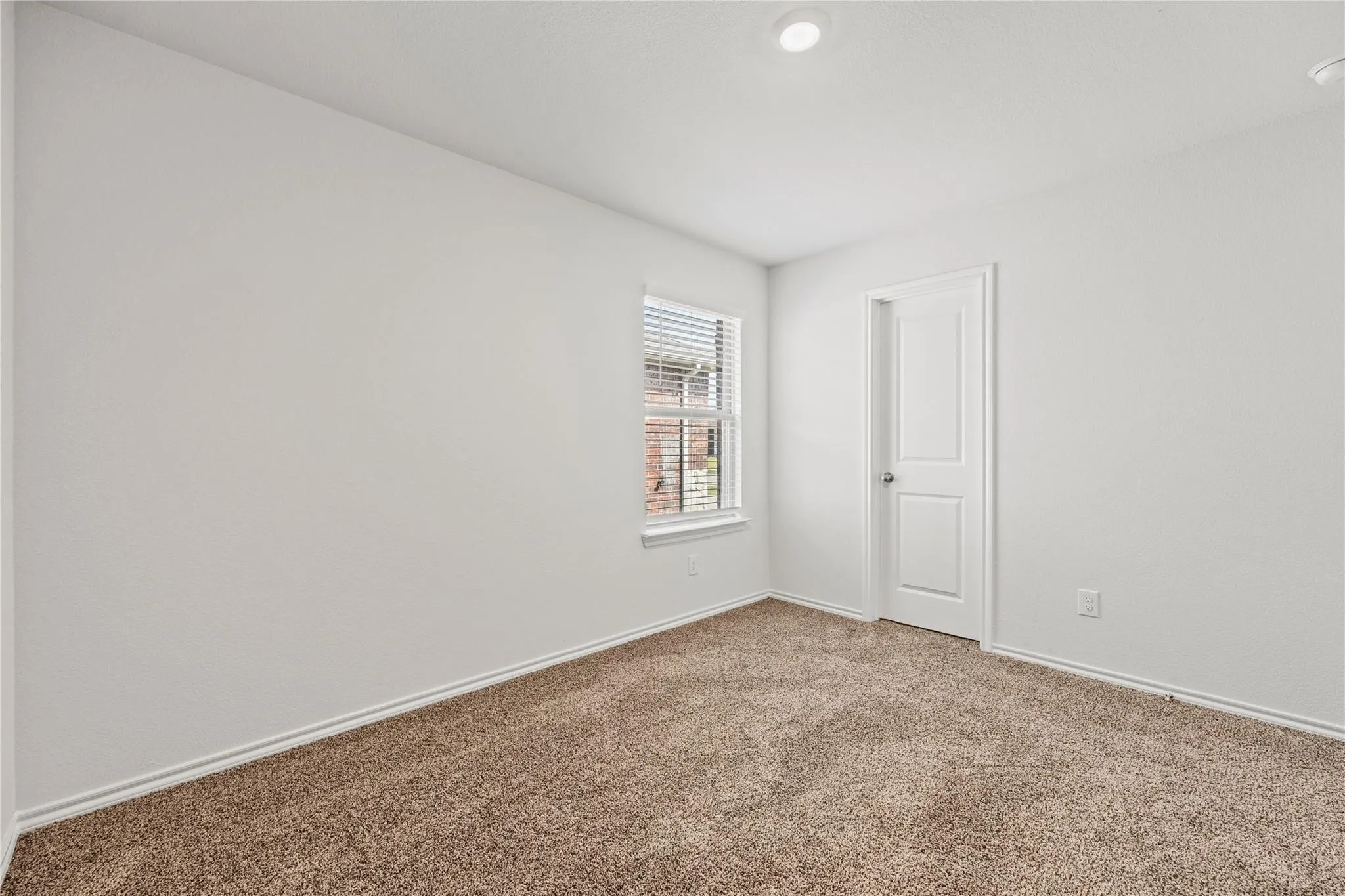 Plush carpet flooring, white painted walls, a single window with blinds, a two-panel interior door, and recessed ceiling lighting