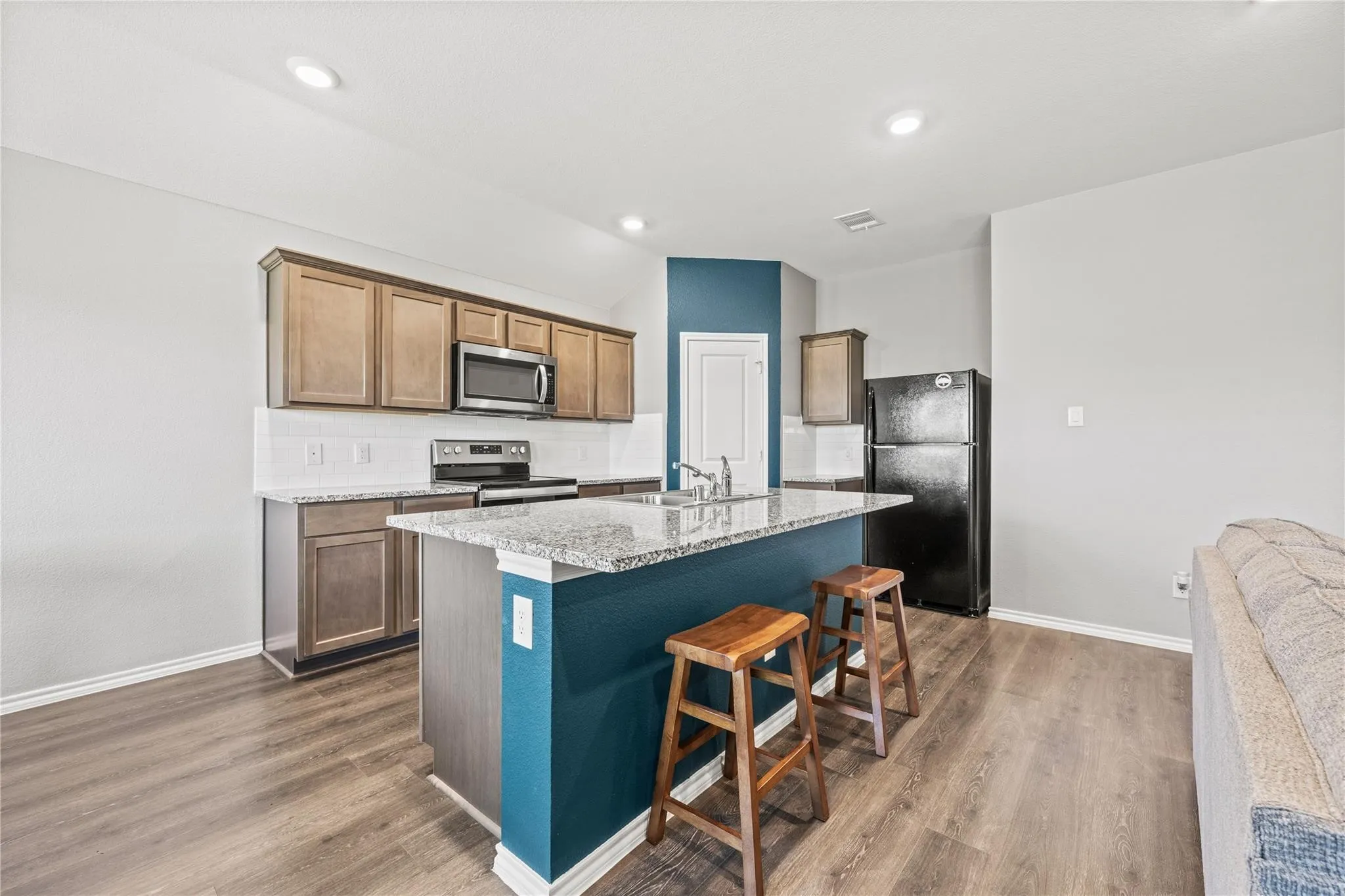 Kitchen featuring a central island with a granite-style countertop, wood-finish flooring, recessed lighting, and stainless steel appliances