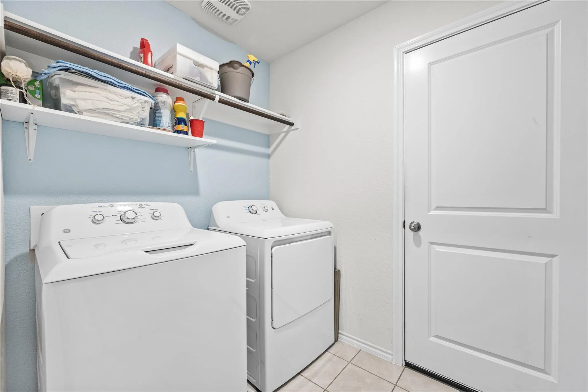 Laundry area featuring a top-load washing machine, front-load dryer, wall-mounted shelving, and tile flooring