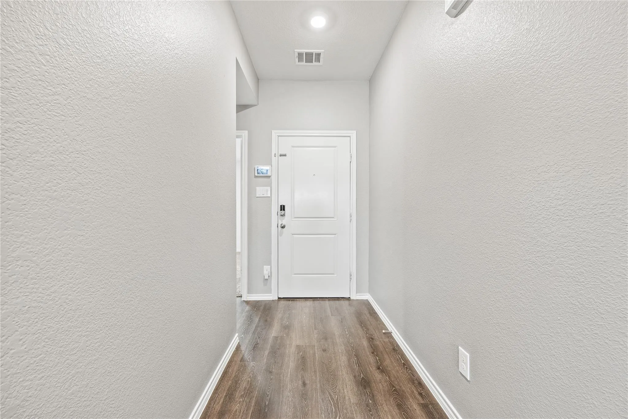 Recessed ceiling lighting, wood-finish flooring, white paneled door, and neutral wall tones
