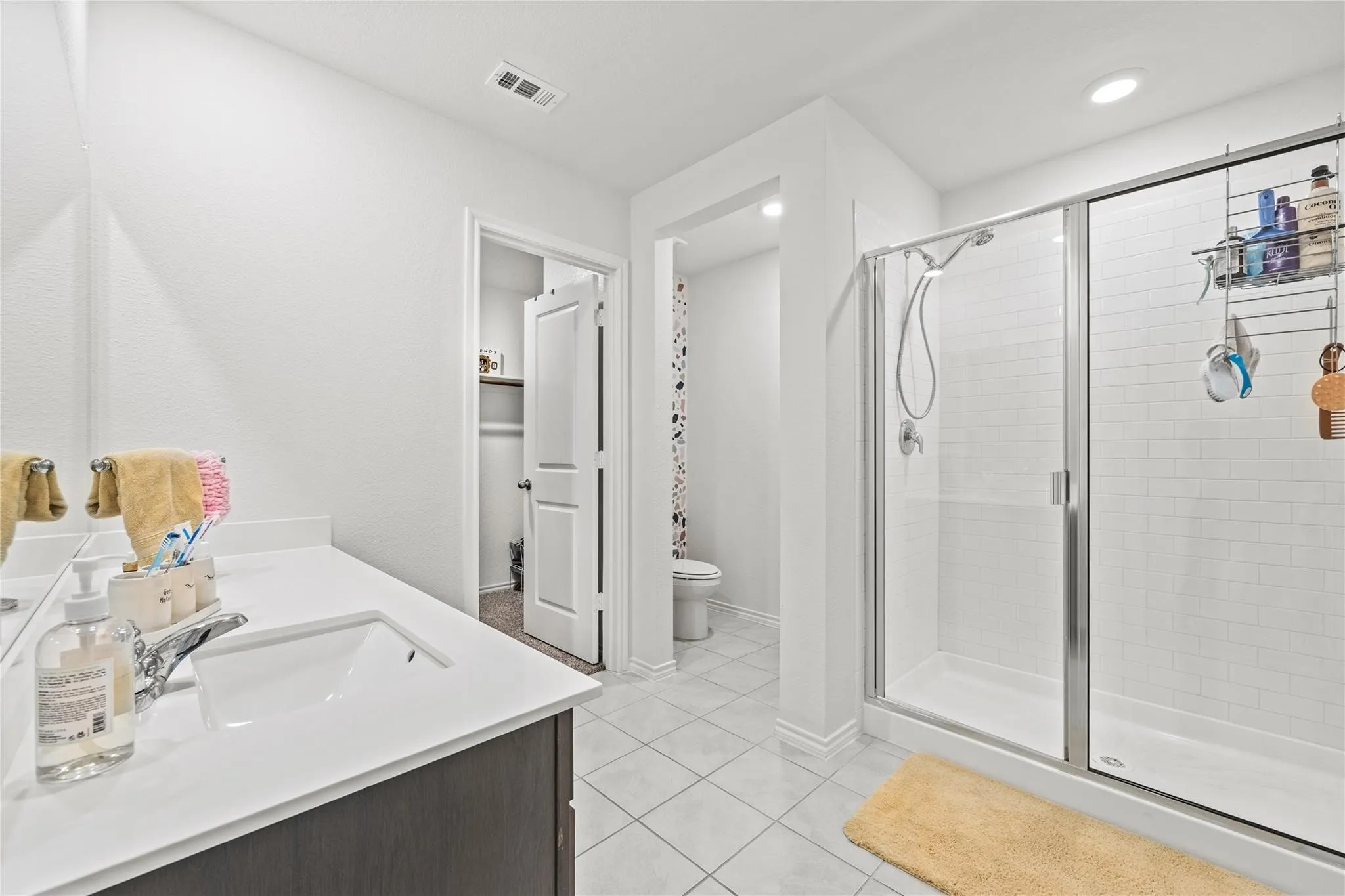 White tile flooring, single vanity with light-toned countertop, walk-in shower with glass enclosure, white subway tile shower surround, and recessed lighting