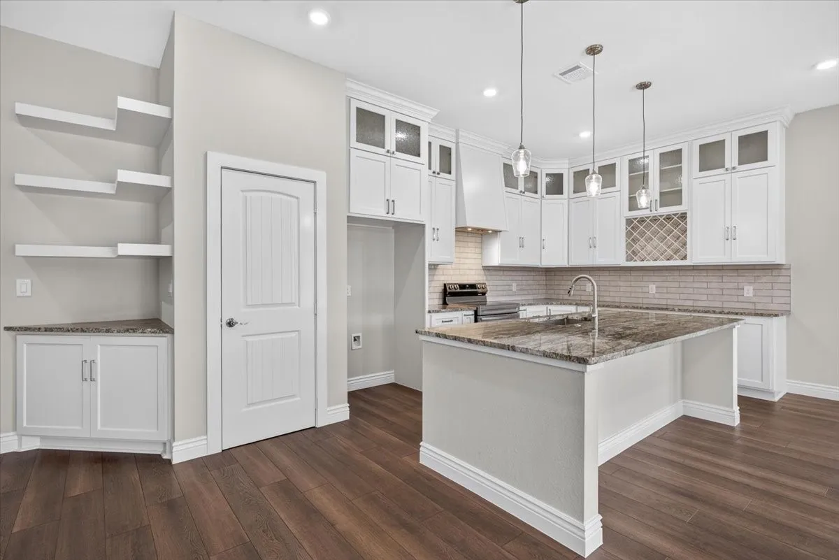 Modern kitchen featuring white cabinetry, a center island with a granite countertop, pendant lighting, and wood-finish flooring